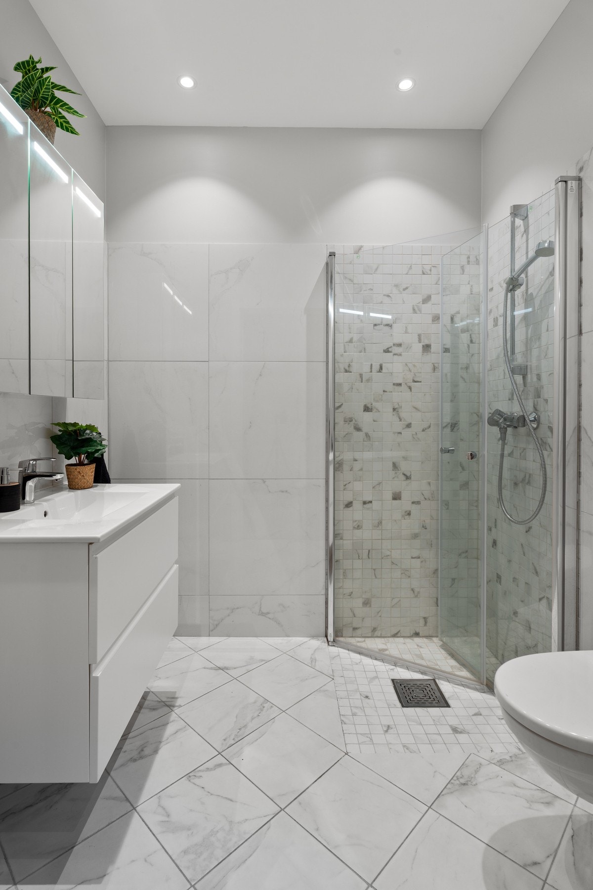 Flislagt og moderne bad med varmekabler i gulv, stilren servantseksjon med skuffer og overskap med speilfronter og integrert belysning. Galleribilde