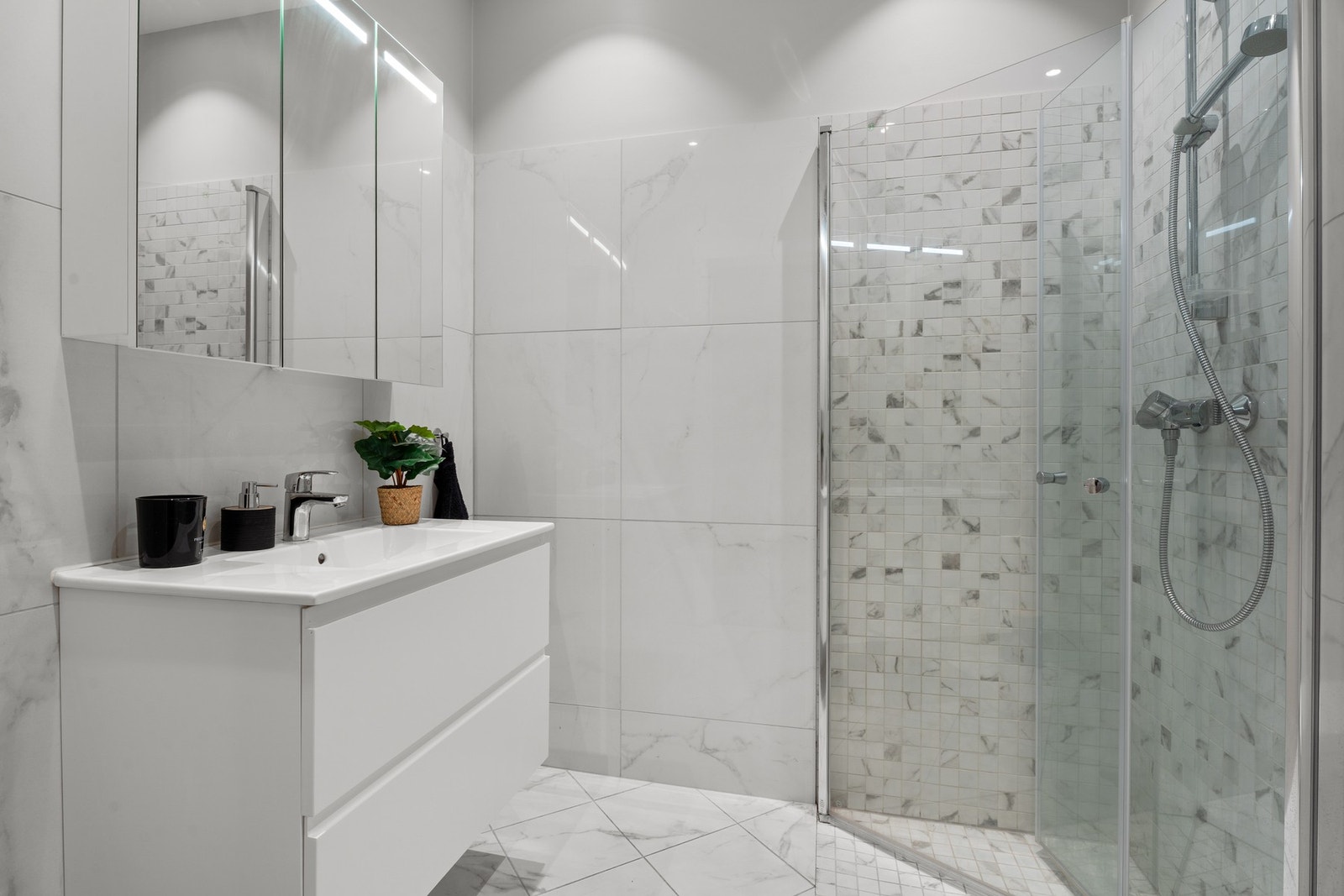 Delikat baderom med nedsenket dusjhjørne med inn-/utadslående glassdører, vegghengt toalett og avtrekk tilkoblet ventilasjonsanlegget. Galleribilde