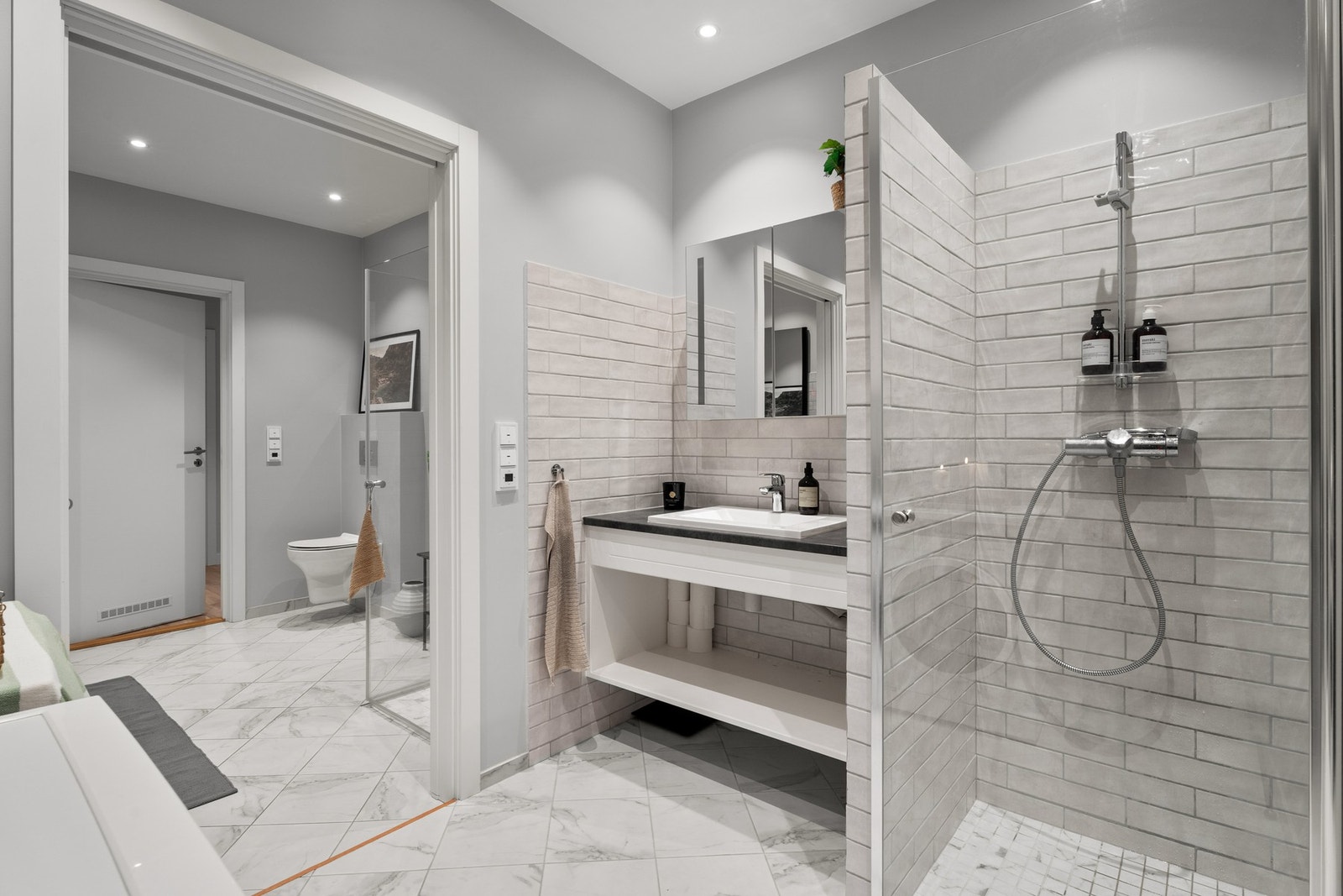 Delikat og romslig bad med dusjnisje, servantseksjon med praktisk hylle og behagelige varmekabler i gulv. Galleribilde