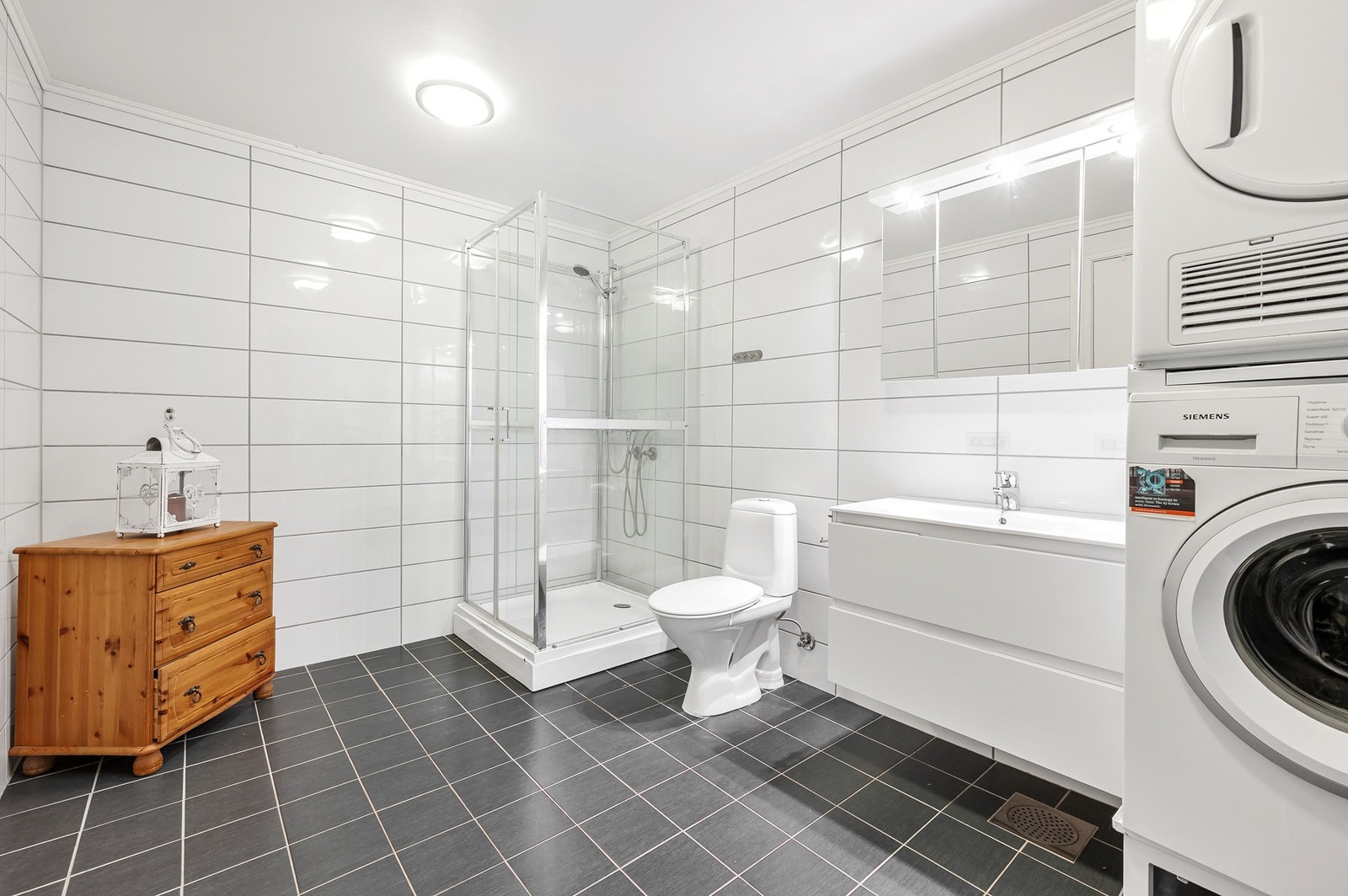 Pent baderom med ekstra bred servant, toalett, dusjkabninett og opplegg for vaskemaskin. Varmekabler i gulvet. Galleribilde