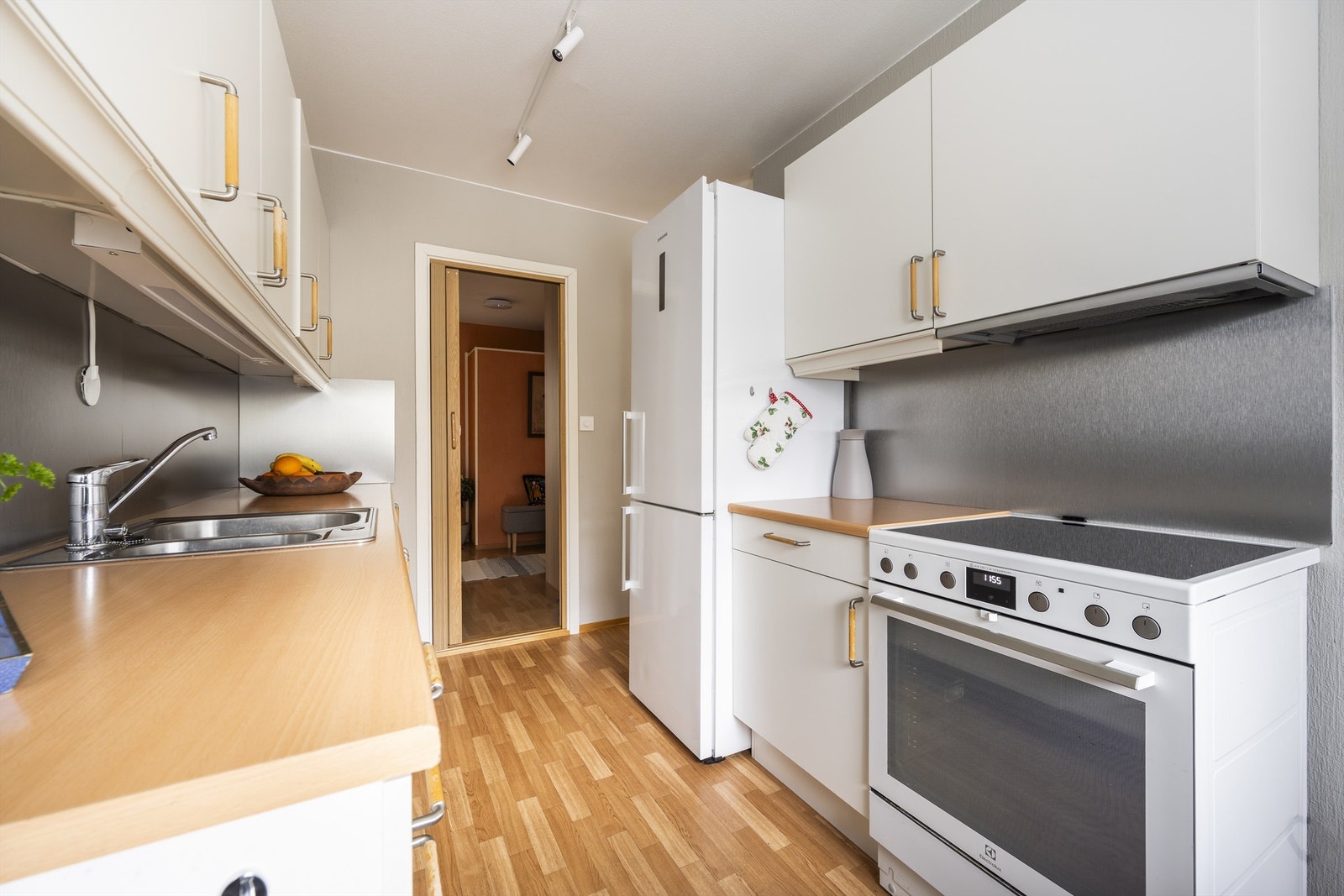 Kjøkkeninnredning med glatte fronter og benkeplate med nedfelt vask. Frittstående kjøleskap, komfyr og oppvaskmaskin medfølger. Kullfilterventilator over kokeplass Galleribilde