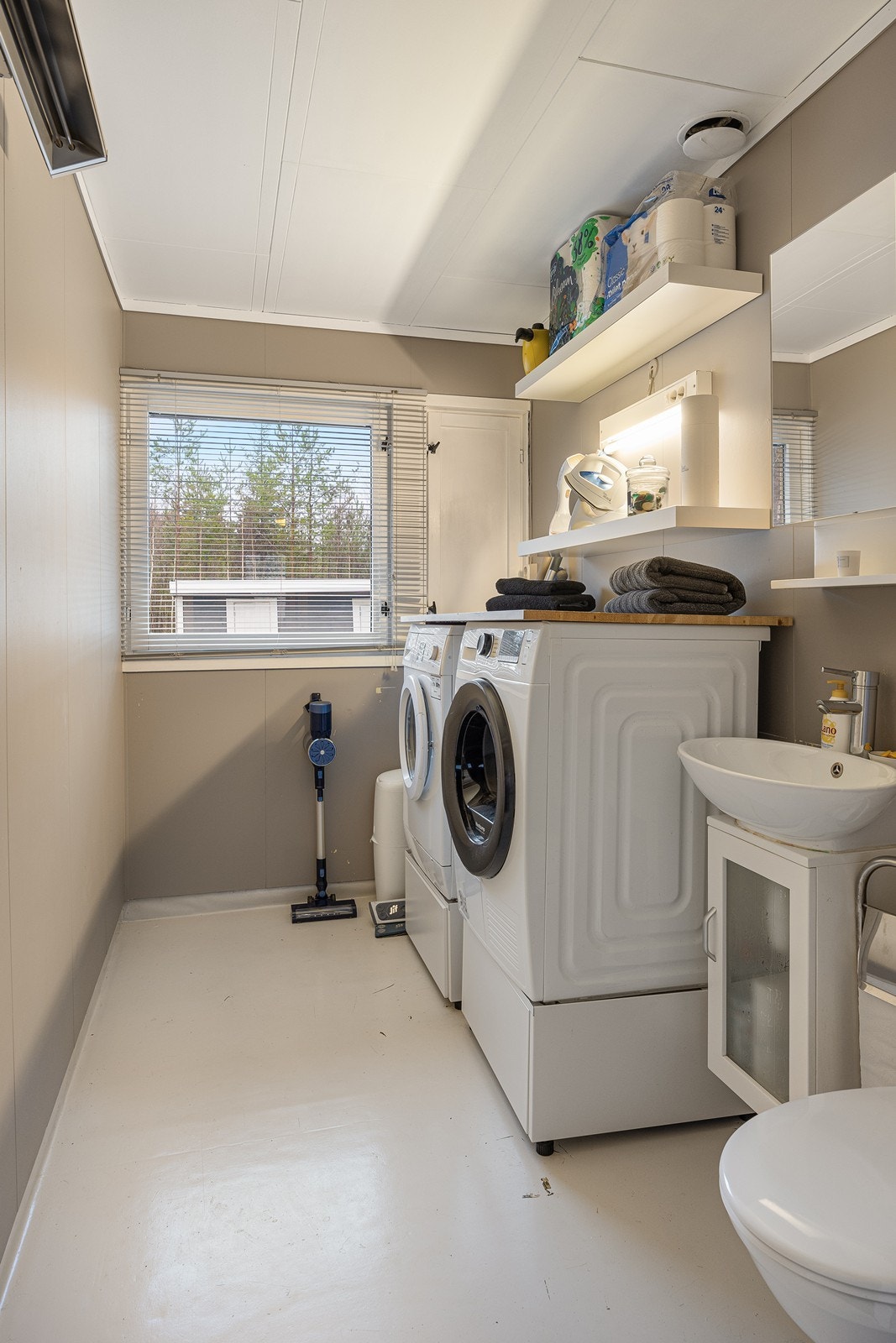 Praktisk vaskerom/toalett med opplegg og plass til vaskemaskin og tørketrommel, samt gulvstående toalett og servant i servantinnredning. Galleribilde