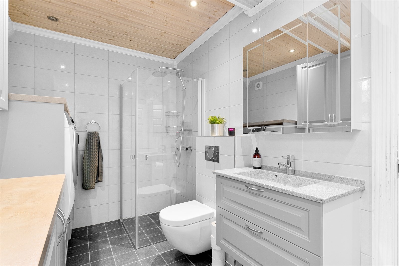 Badet nede er et kombinert bad og vaskerom, modernisert i 2014. Her har man regndusj med glassvegger, heldekkende servant med overskap, samt innebygget sisterne til et vegghengt toalett. Galleribilde