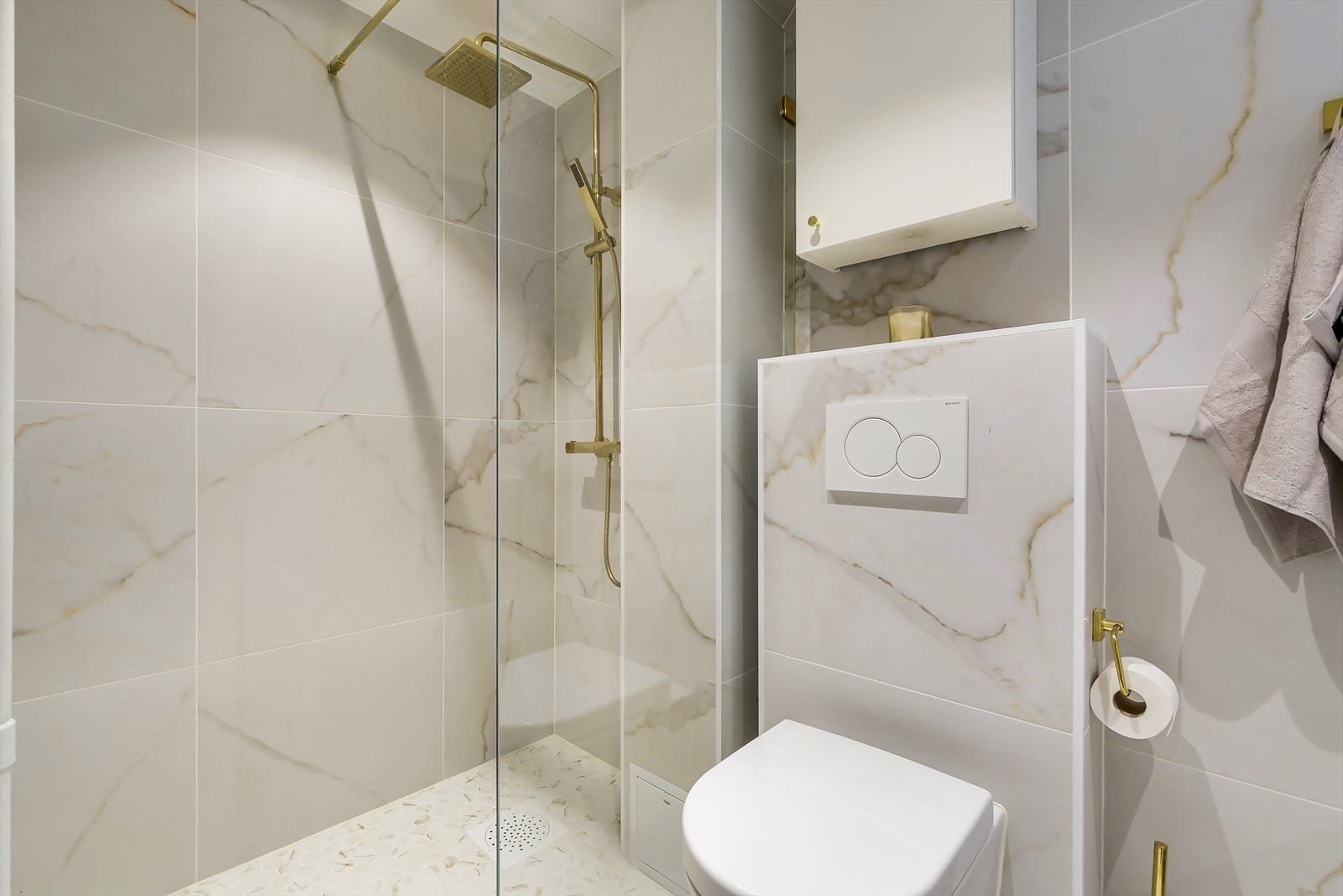 Badet er utstyrt med et veggmontert toalett, et dusjhjørne med glassvegg og stang for dusjforheng. Servantinnredning med nisje til grunn vaskemaskin. Galleribilde