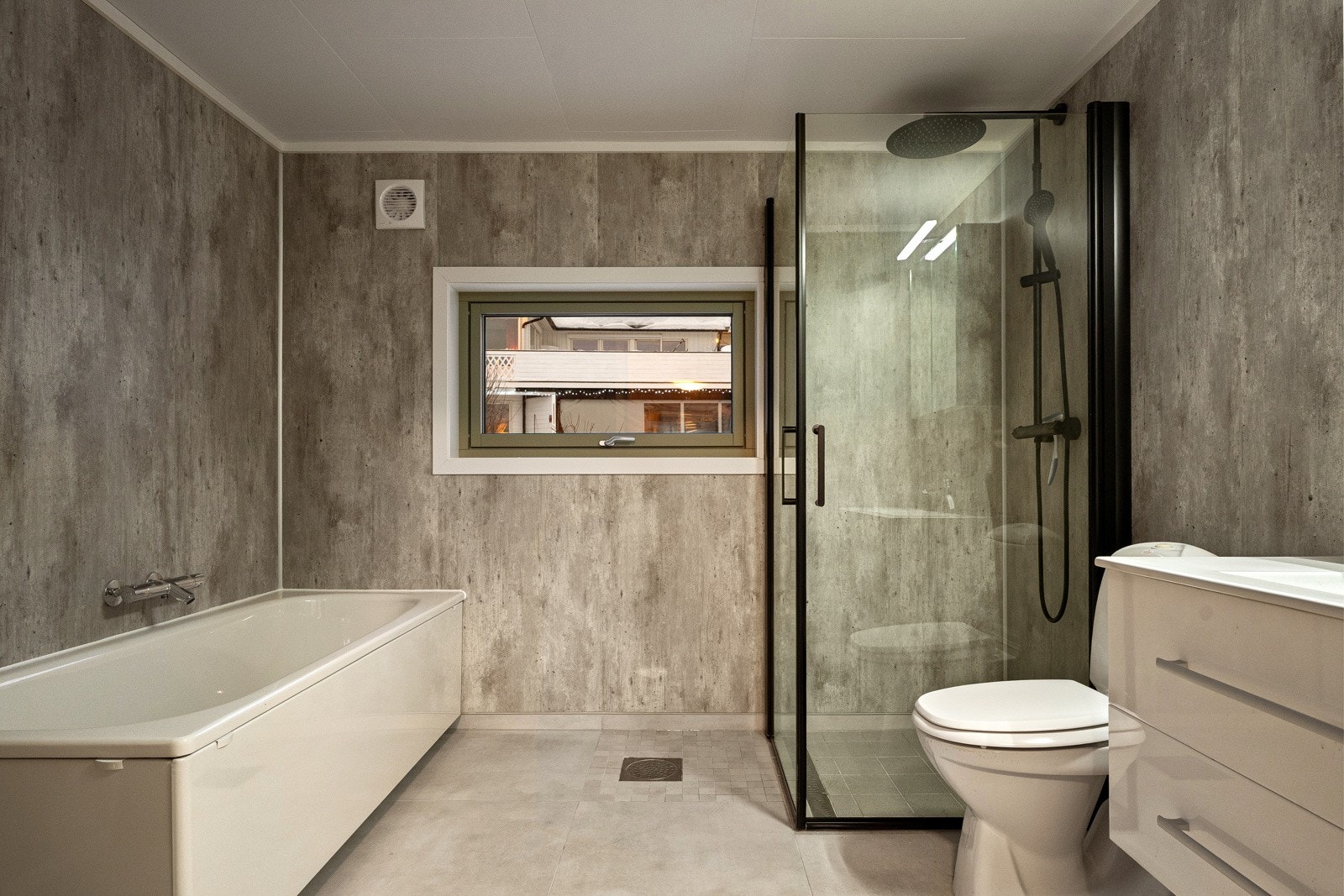 Baderommet er innredet med dusjvegger med dusjgarnityr på vegg, badekar, vegghengt servant og speil med belysning.