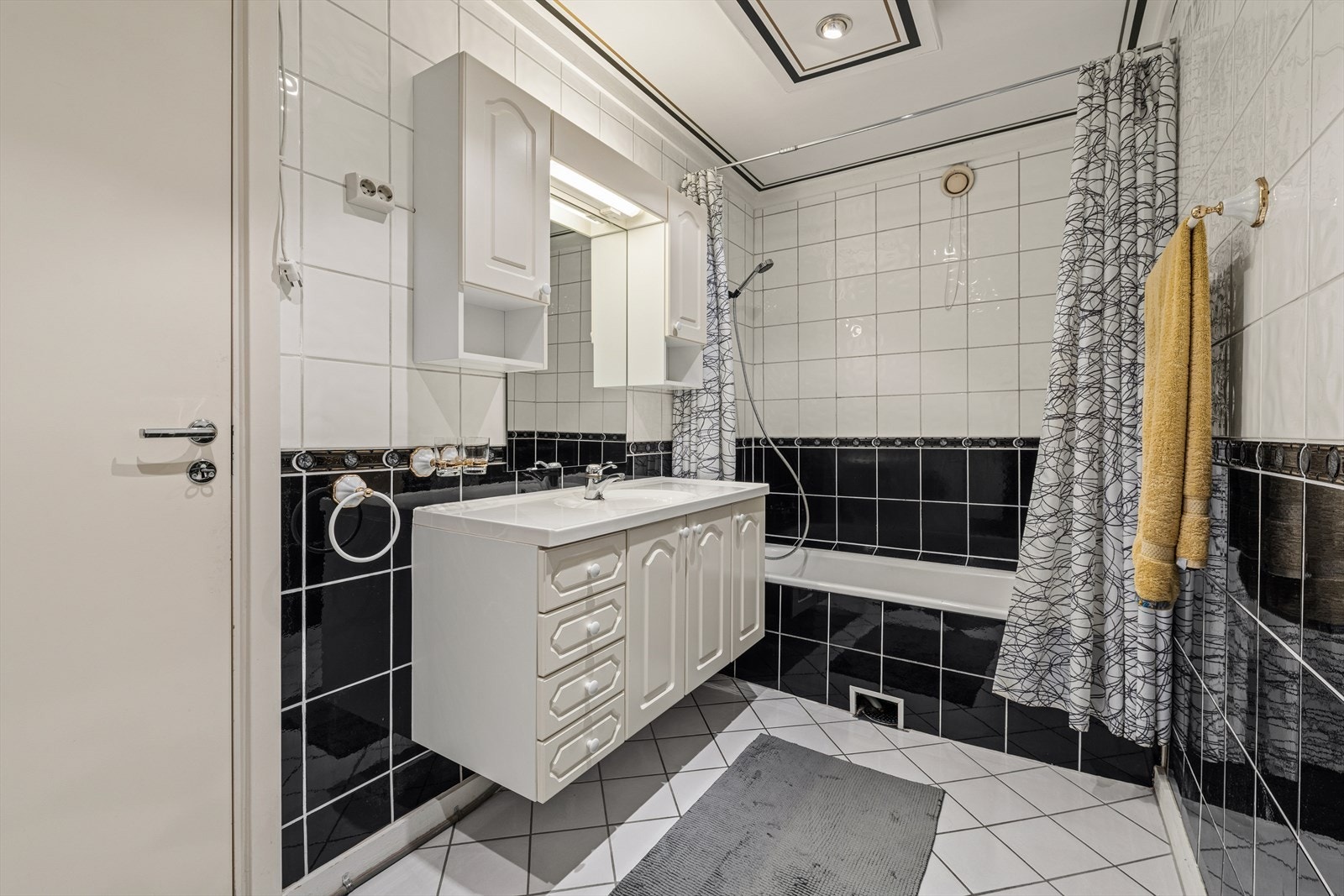 Bad/vaskerom med flislagt gulv og fliskledde vegger, innredet med romslig servantseksjon, speilskap og innbygd badekar med dusjløsning. Galleribilde