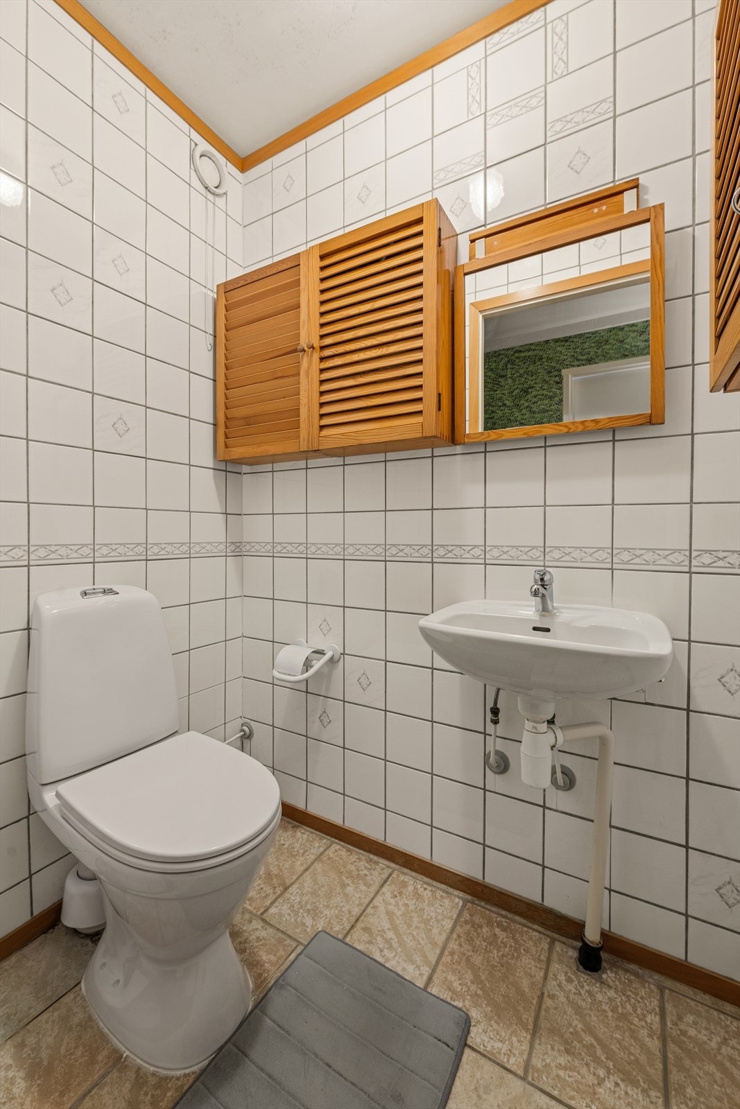 Separat toalettrom med flislagt gulv og fliskledde vegger samt malt betonghimling. Rommet er innredet med gulvmontert toalett og vegghengt servant med ettgreps armatur. Galleribilde