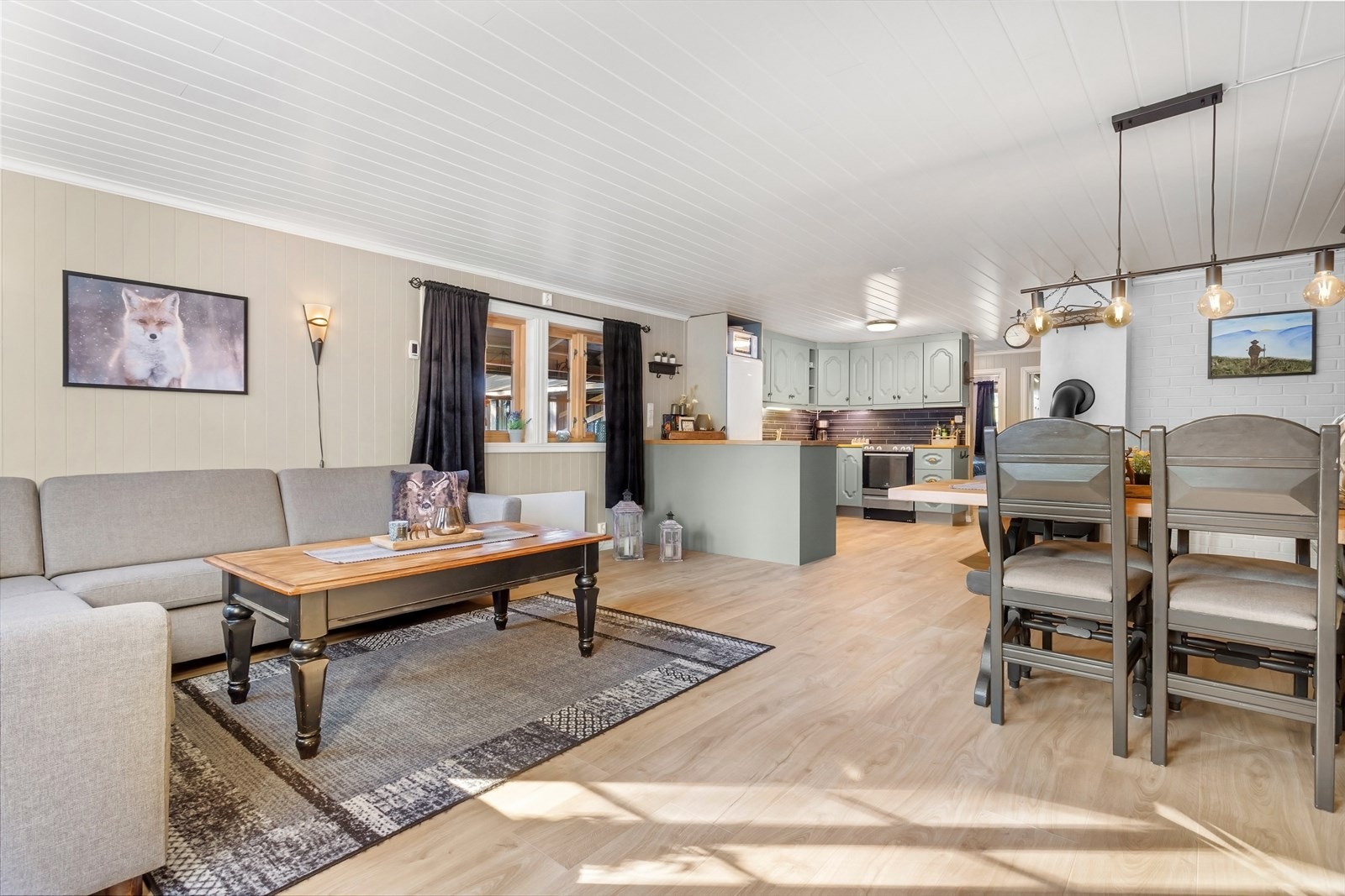 Lys og innbydende stue med 1-stavs laminat på gulv og panel på vegg malt i lyse fargetoner. Galleribilde