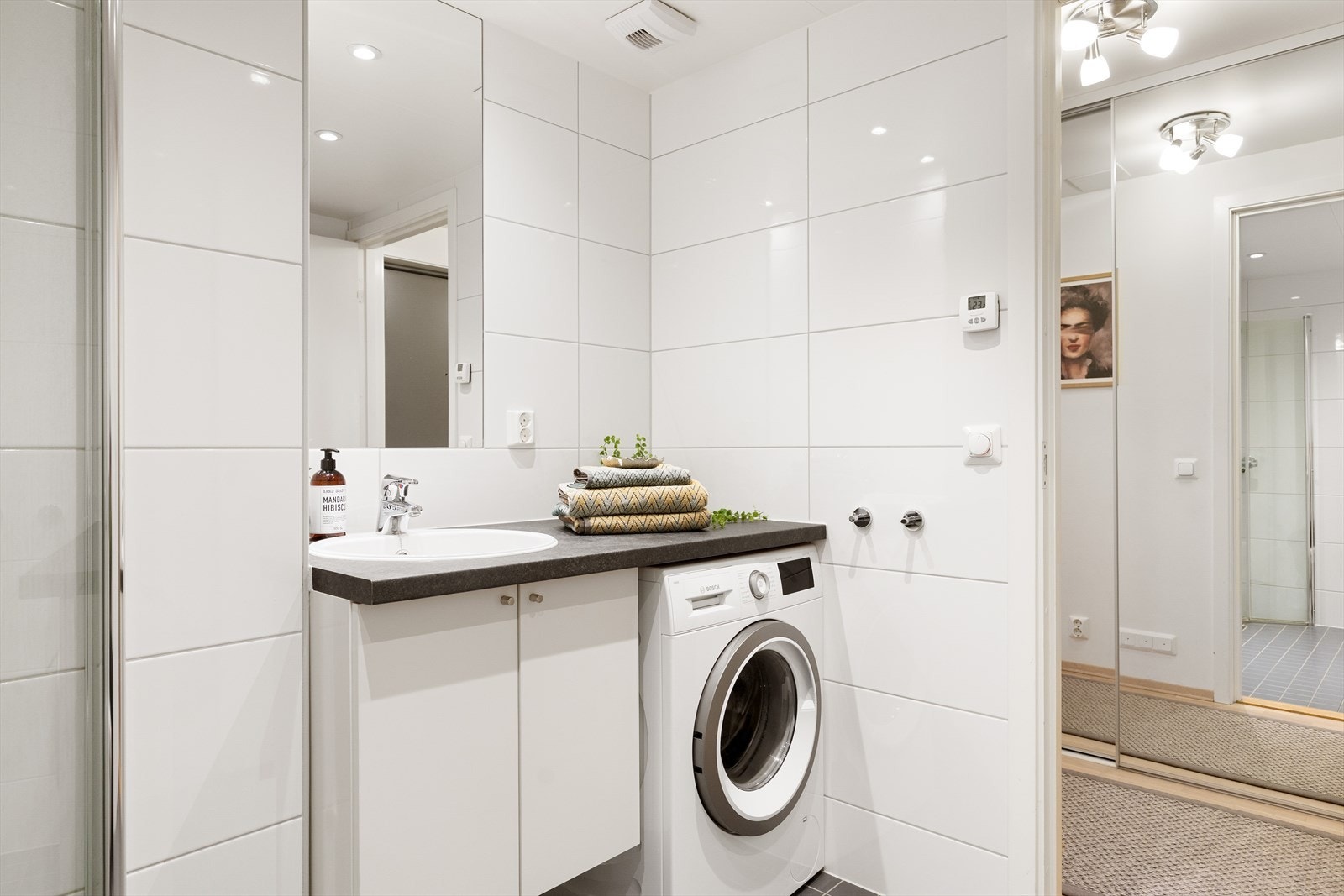 Badet er innredet med benkeplate med servantskap og nedfelt servant, innmurt speil, vegghengt toalett samt dusjhjørne med svingdører i herdet glass. Det er opplegg for vaskemaskin. Galleribilde