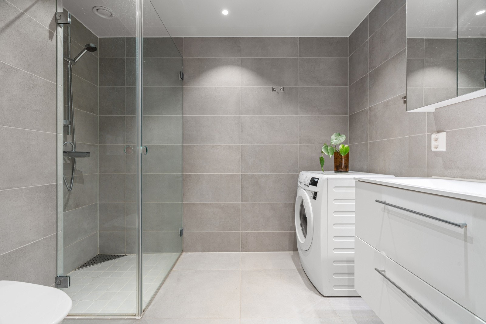 Delikat bad med grå fliser, varme i gulvet og god plass for vaskemaskin. Galleribilde