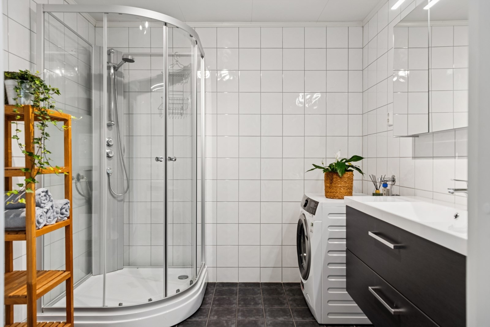 Baderommet har fliser på gulv og vegger. Det er ellers innredet med servantskap, speilskap, dusjkabinett, toalett og det er opplegg for vaskemaskin. Galleribilde