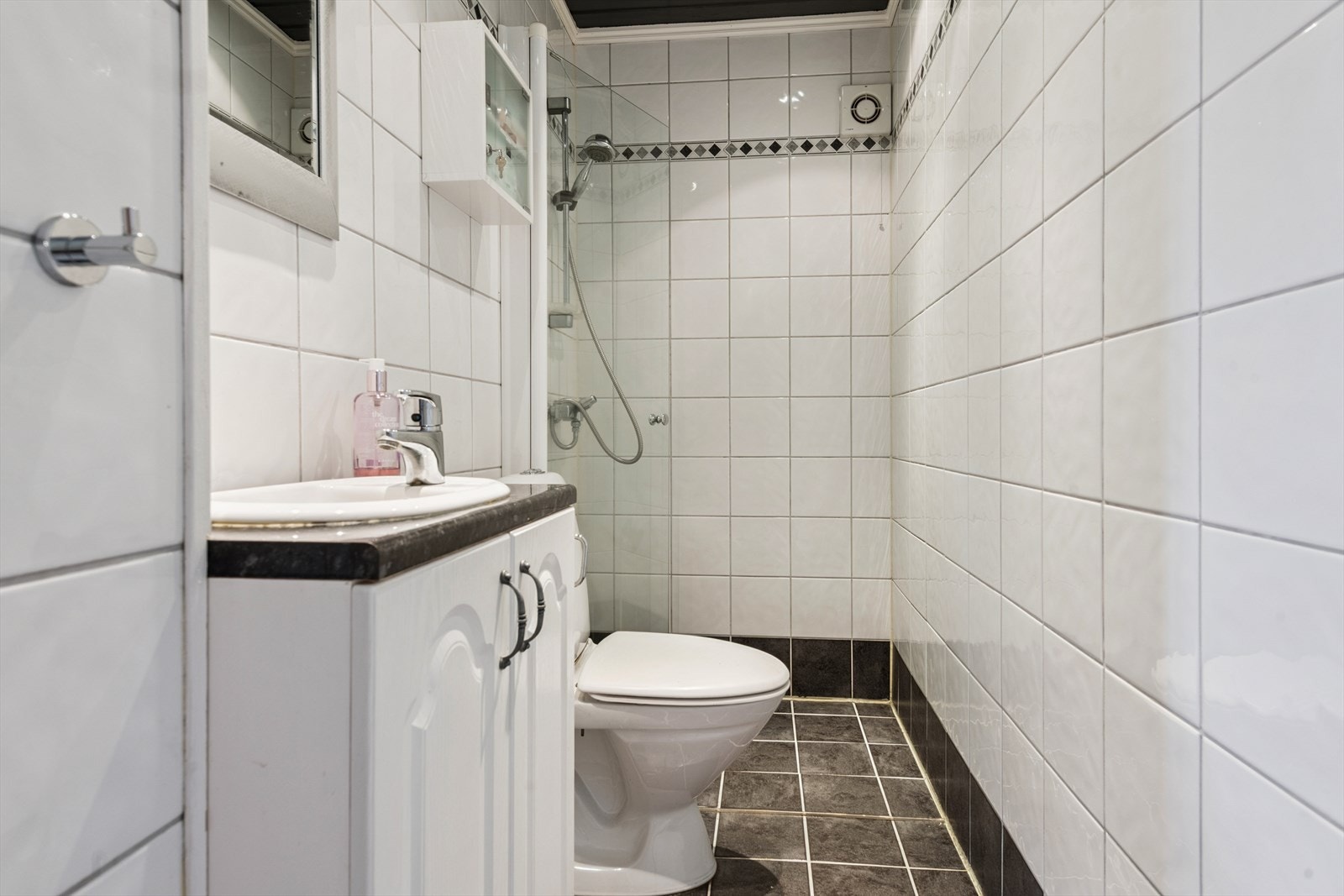 Hvitt flislagt baderom fra 2010 med gulvvarme. Inneholder servant i baderomsinnredning, toalett og dusjhjørne med innfellbar glassdør. Galleribilde