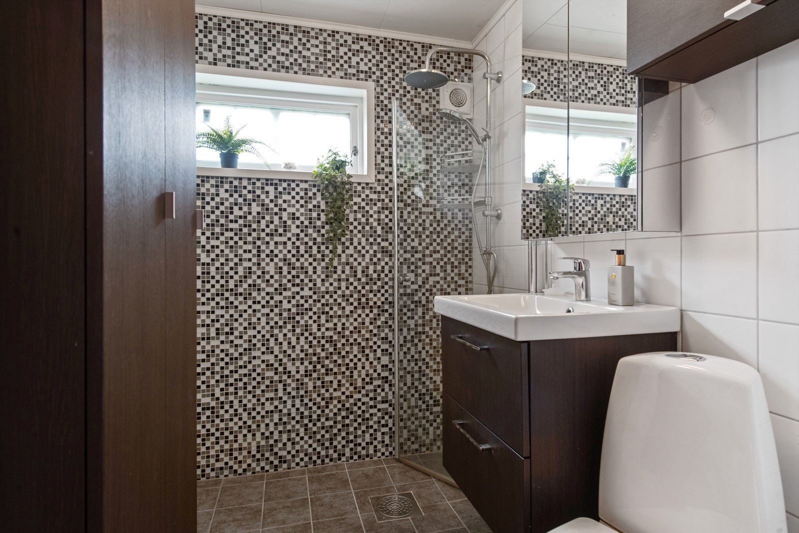 Mørk flislagt baderom fra 2015 med gulvvarme. Inneholder servant i baderomsinnredning, toalett, regnfallsdusj i hjørne med innfellbar glassdør. Her er det opplegg for vaskemaskin. Galleribilde