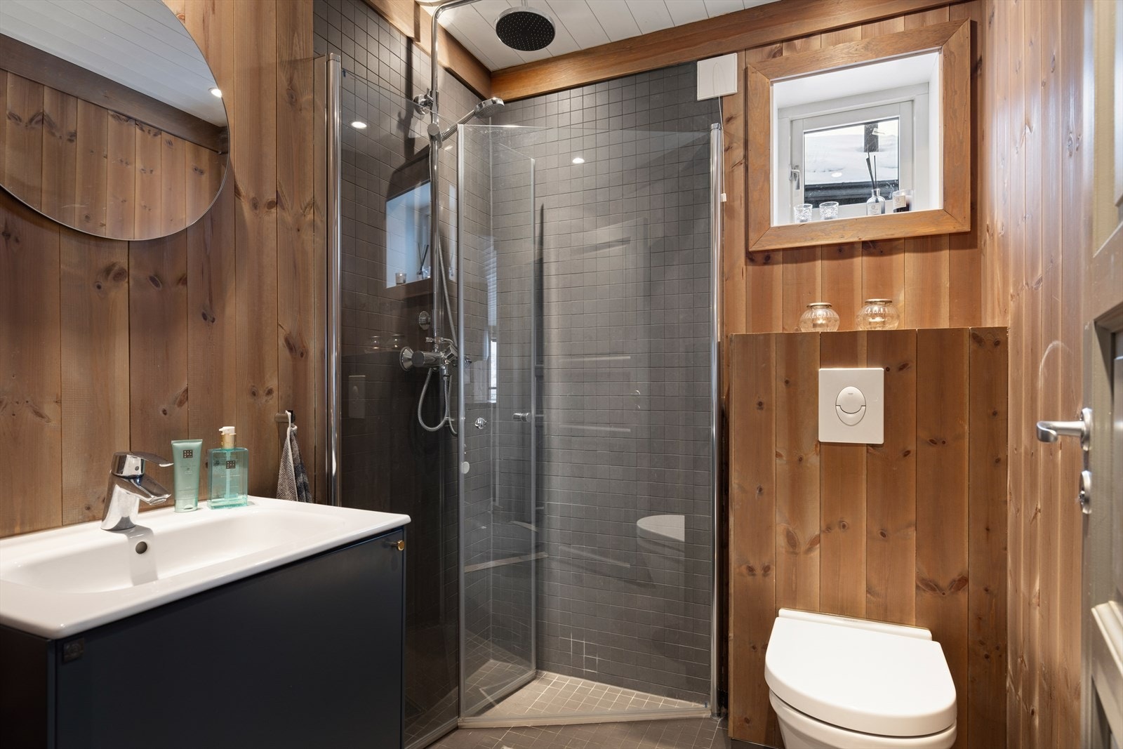 Delikat baderom med flislagt gulv og panel på veggene, som gir et moderne og lunt uttrykk. Praktisk utformet med dusjhjørne og god plass. Galleribilde