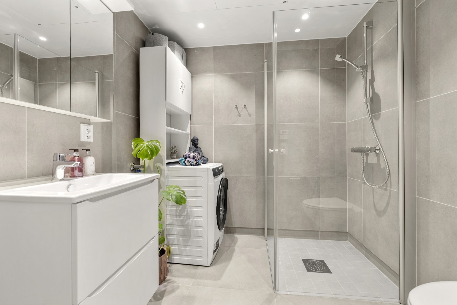 Moderne, flislagt bad fra 2024 med dusjhjørne og opplegg for vaskemaskin. Galleribilde