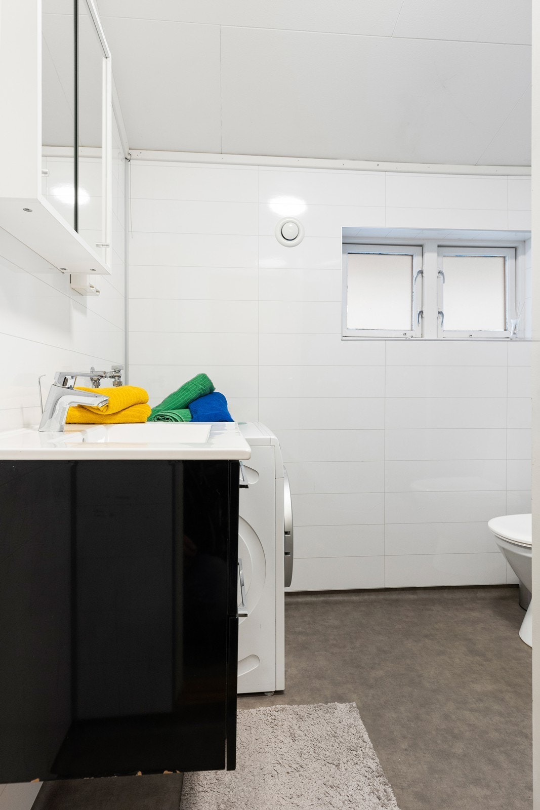 Bad har vinylbelgg på gulv, baderomsplater med hvit flisemønster på vegg og himlingsplater i tak. Galleribilde