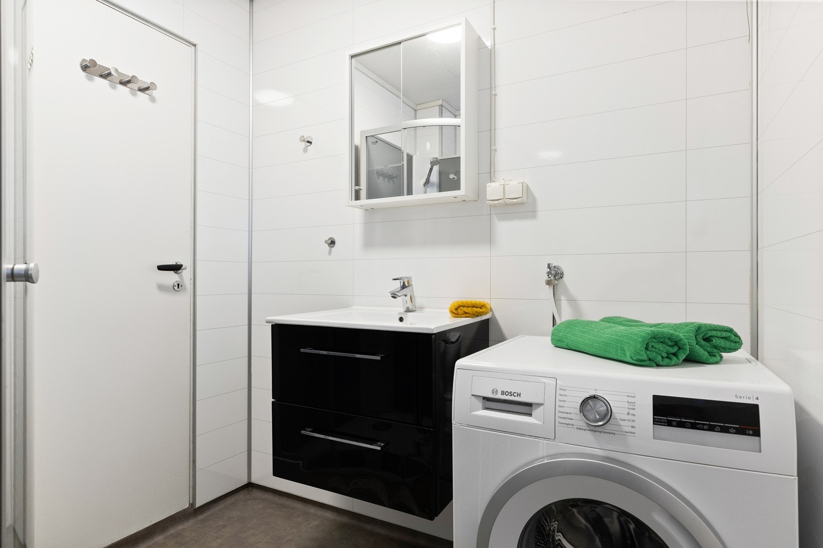 Badet er praktisk innredet med sort baderomsinnredning med skuffer for oppbevaring og heldekkende servant. Speilsskap over baderomsinnredning. Videre er rommet innredet med dusjkabinett og gulvmontert toalett. Opplegg for vaskemaskin på bad. Galleribilde