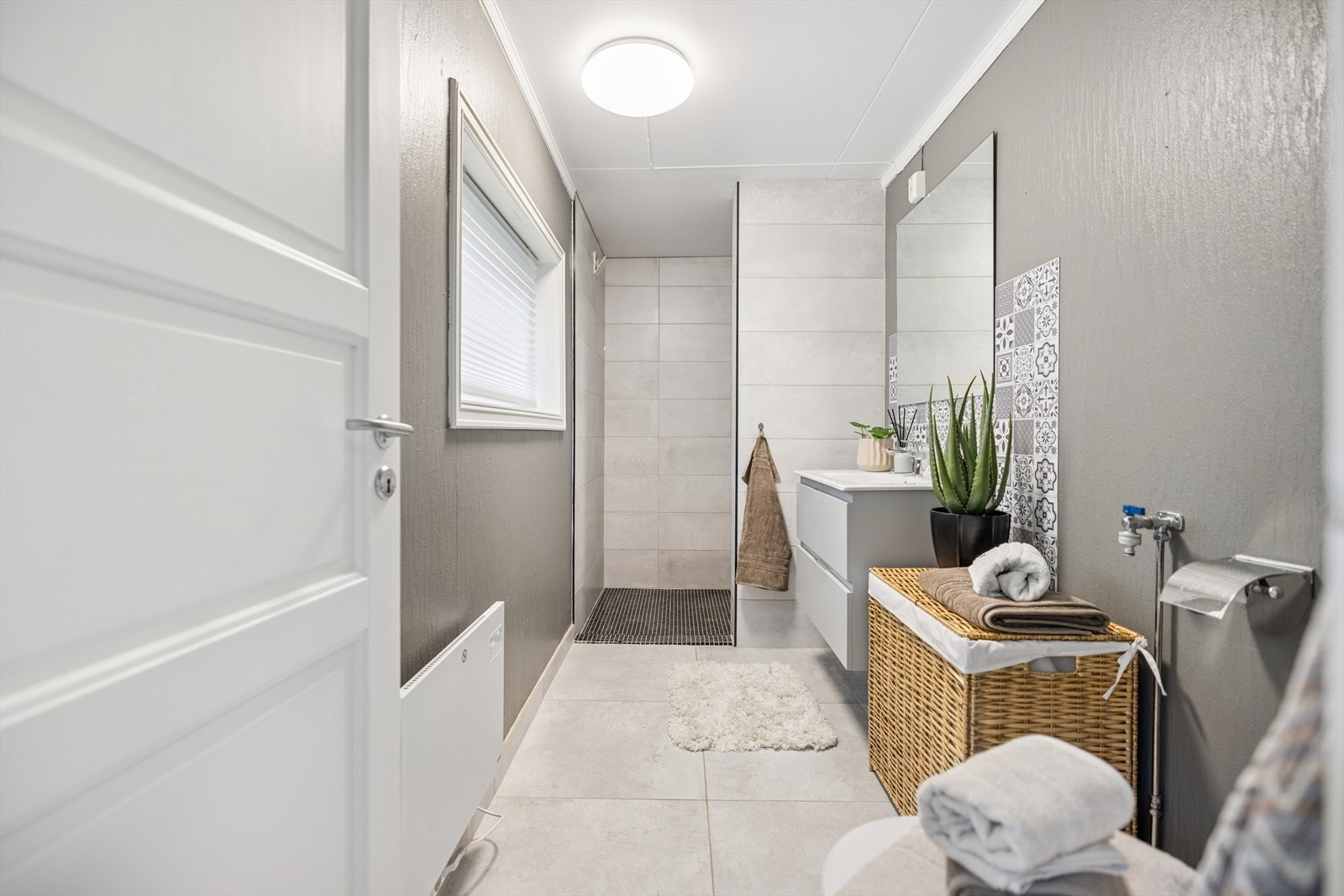 Badet har flislagt gulv, dusjhjørne og praktisk opplegg for vaskemaskin. Galleribilde