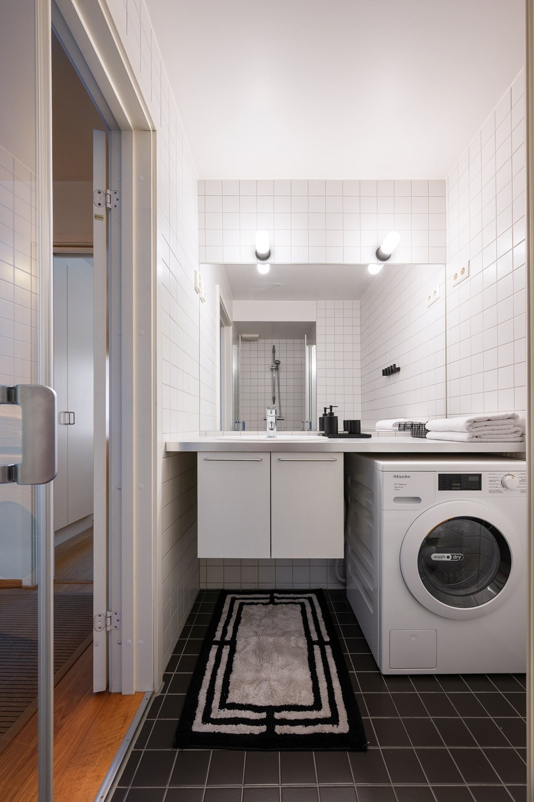 Badet er innredet med vegghengt servantinnredning med nedfelt vask i benkeplate, speil med lys og stikkontakt over servant og veggfestet toalett. Galleribilde