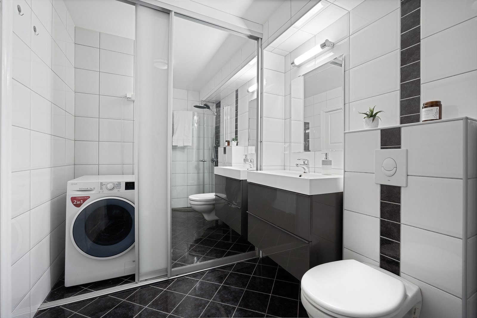 Badet har en praktisk løsning hvor opplegg for vaskemaskin og tørketrommel er skjult, og gir ekstra oppbevaring på badet. Galleribilde