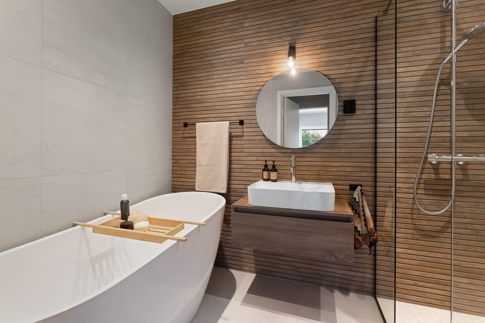 Badet vis-a-vis soverommet fremstår svært delikat med spilefliser, badekar, toppmontert servant med rundt speil og belysning over, samt dusjhjørne med glassdører. Galleribilde