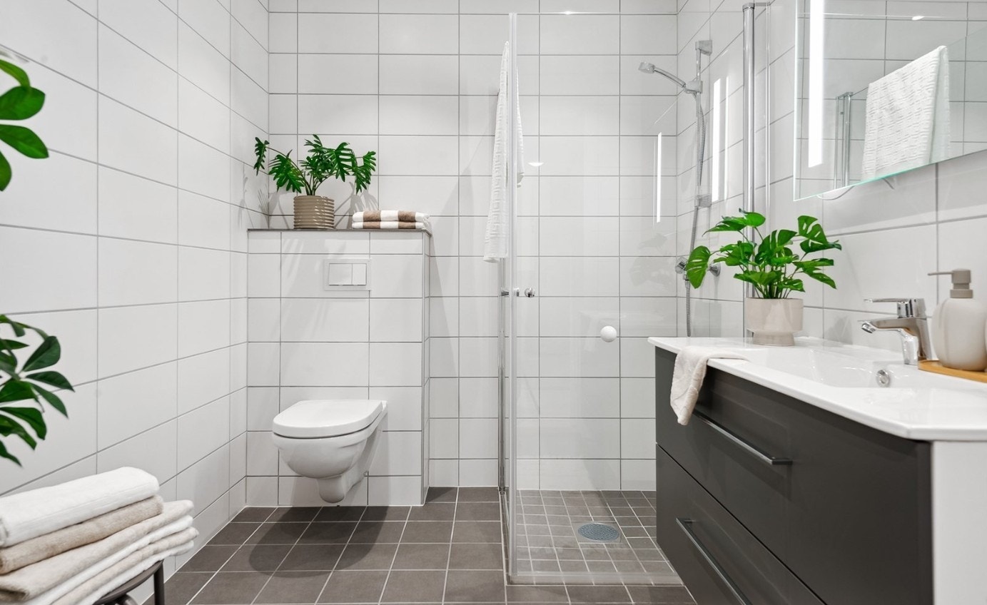 Flislagt bad med moderne innredning som heldekkende servant, dusjhjørne med glassdører og toalett. Galleribilde