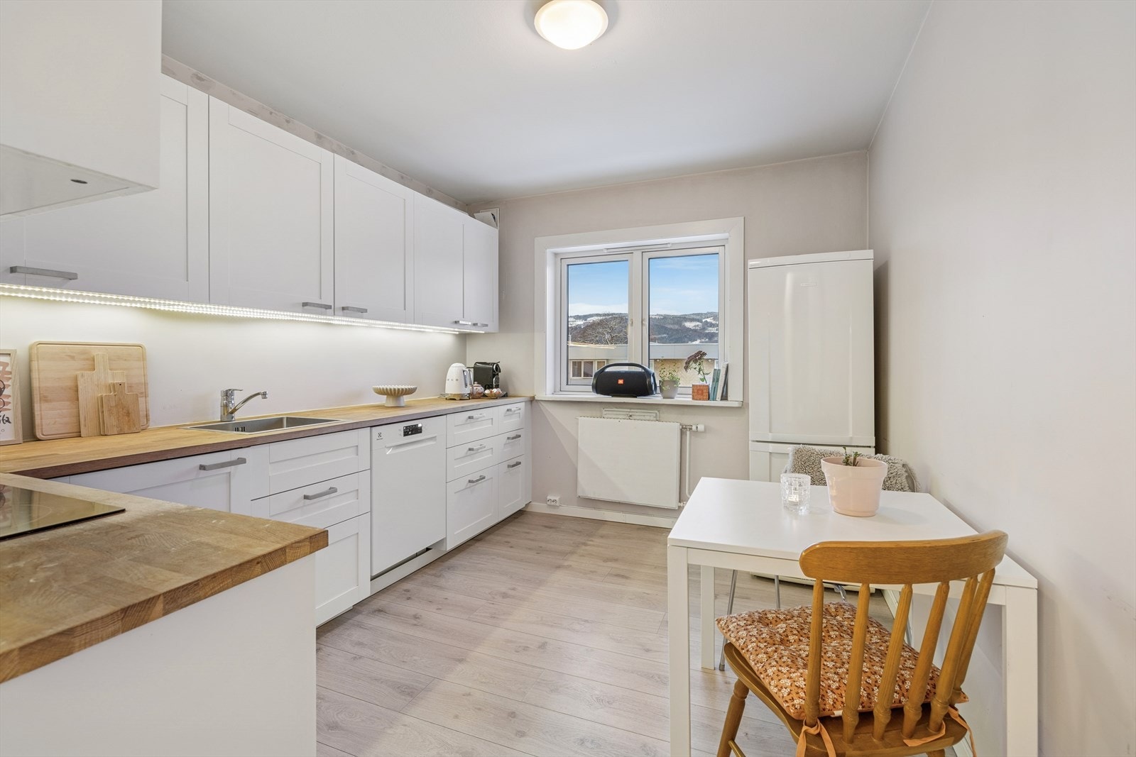 Delikat kjøkken med hvite profilerte fronter og heltre benkeplate med kjøkkenkum. Galleribilde