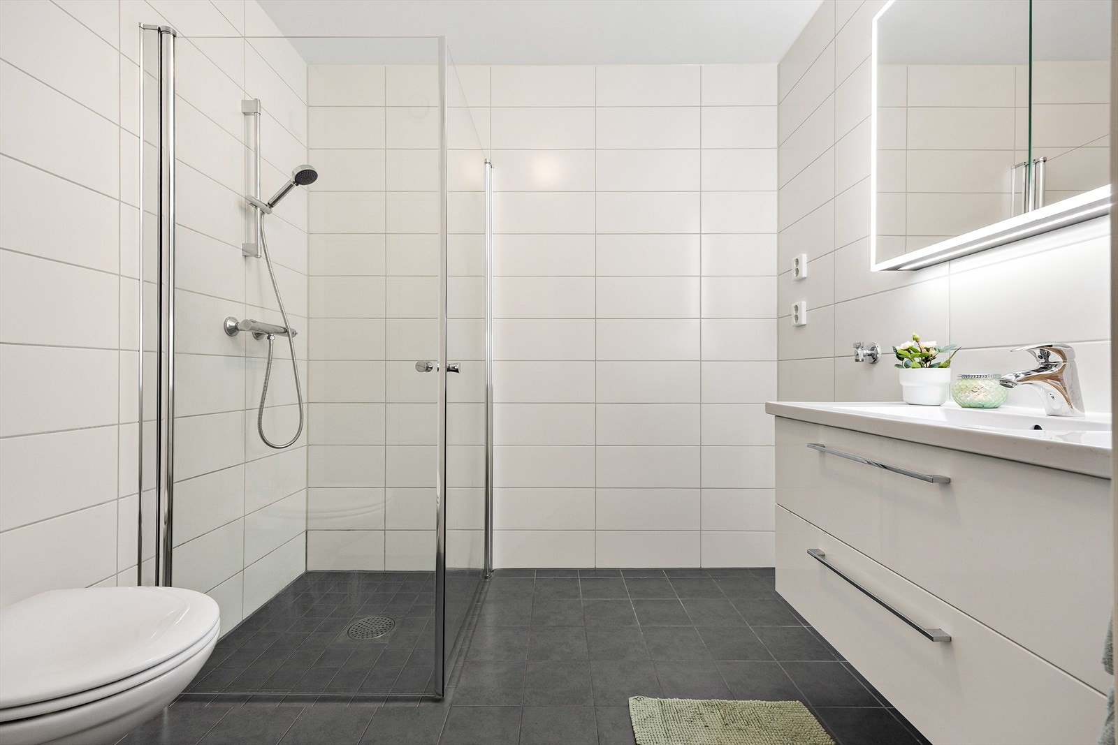 Leiligheten har et romslig, pent og praktisk bad med hvite fliser på veggene og grå fliser på gulv med gulvvarme. Galleribilde