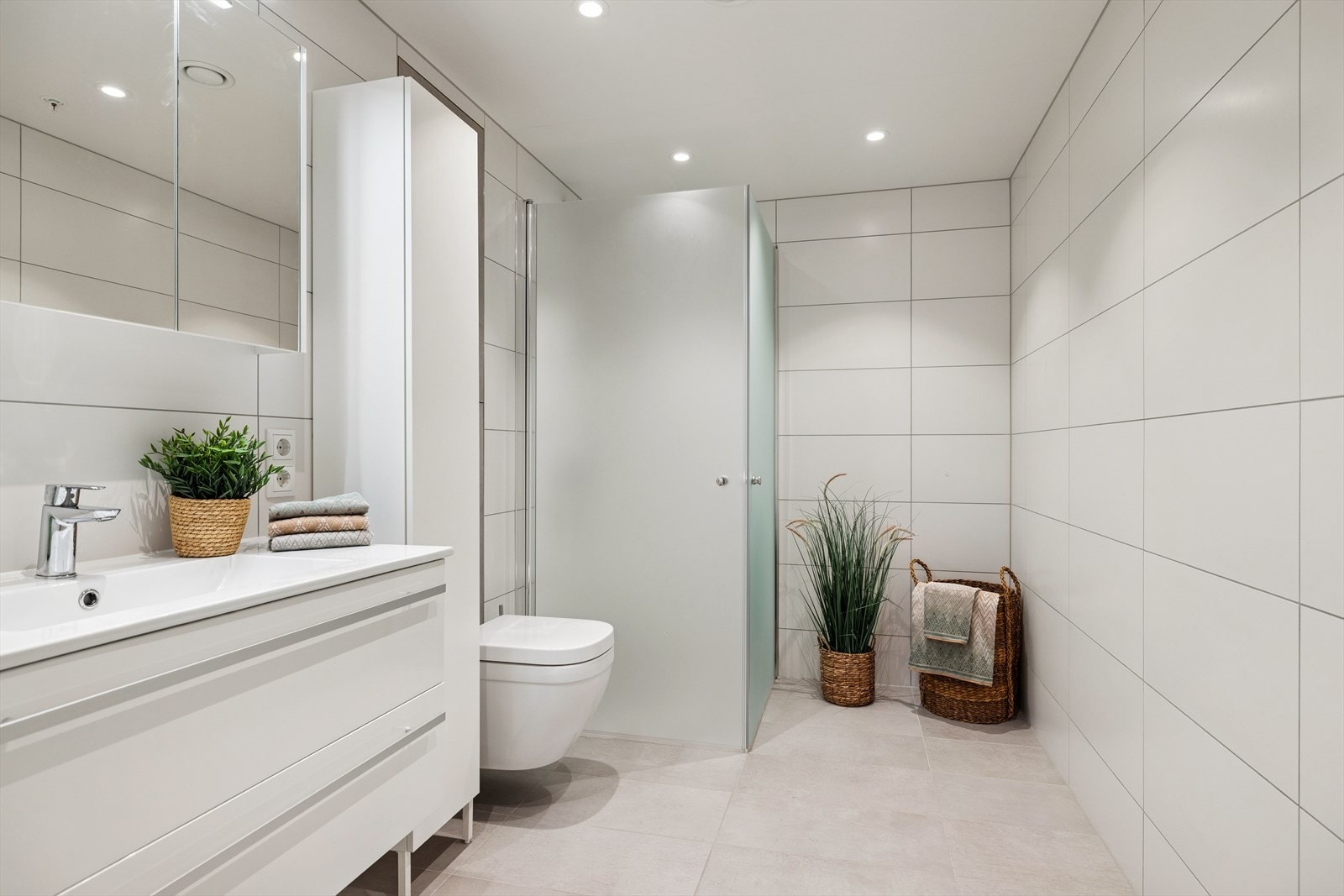 Flislagt bad med varmekabler, veggmontert toalett, dusjhjørne og moderne innredning. Galleribilde