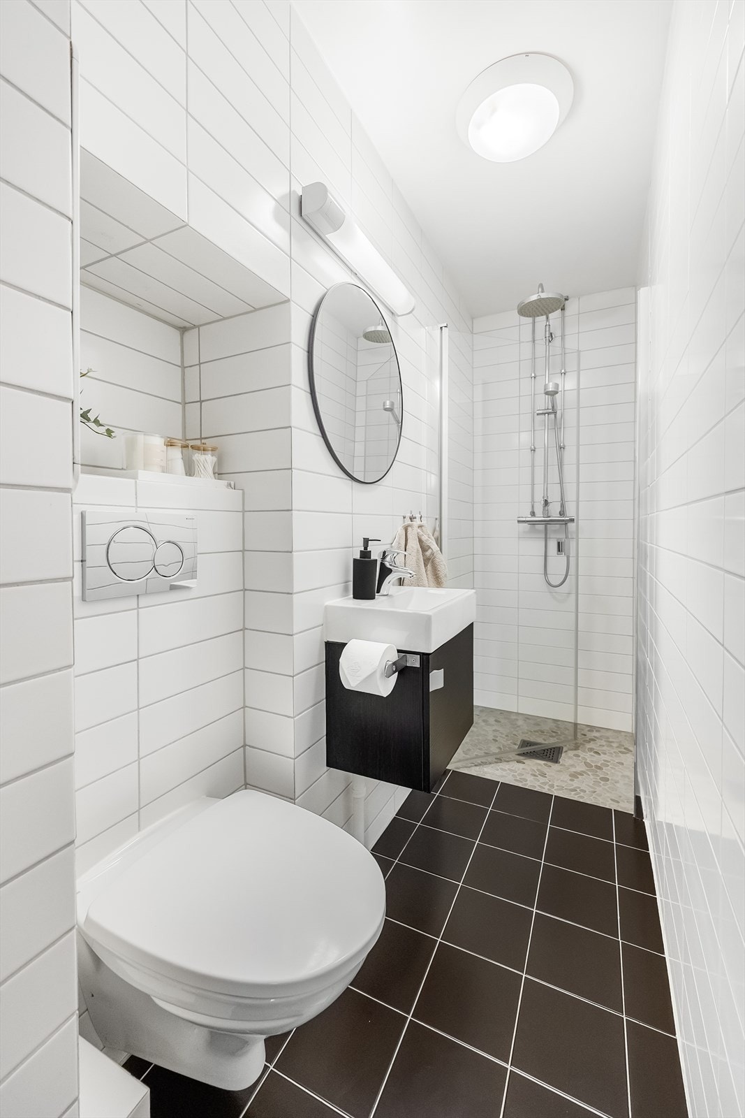 Videre er badet utstyrt med vegghengt toalett med innebygget sisternekasse og dusj med glassdør, tilkoblet hånddusj og regndusj. Galleribilde