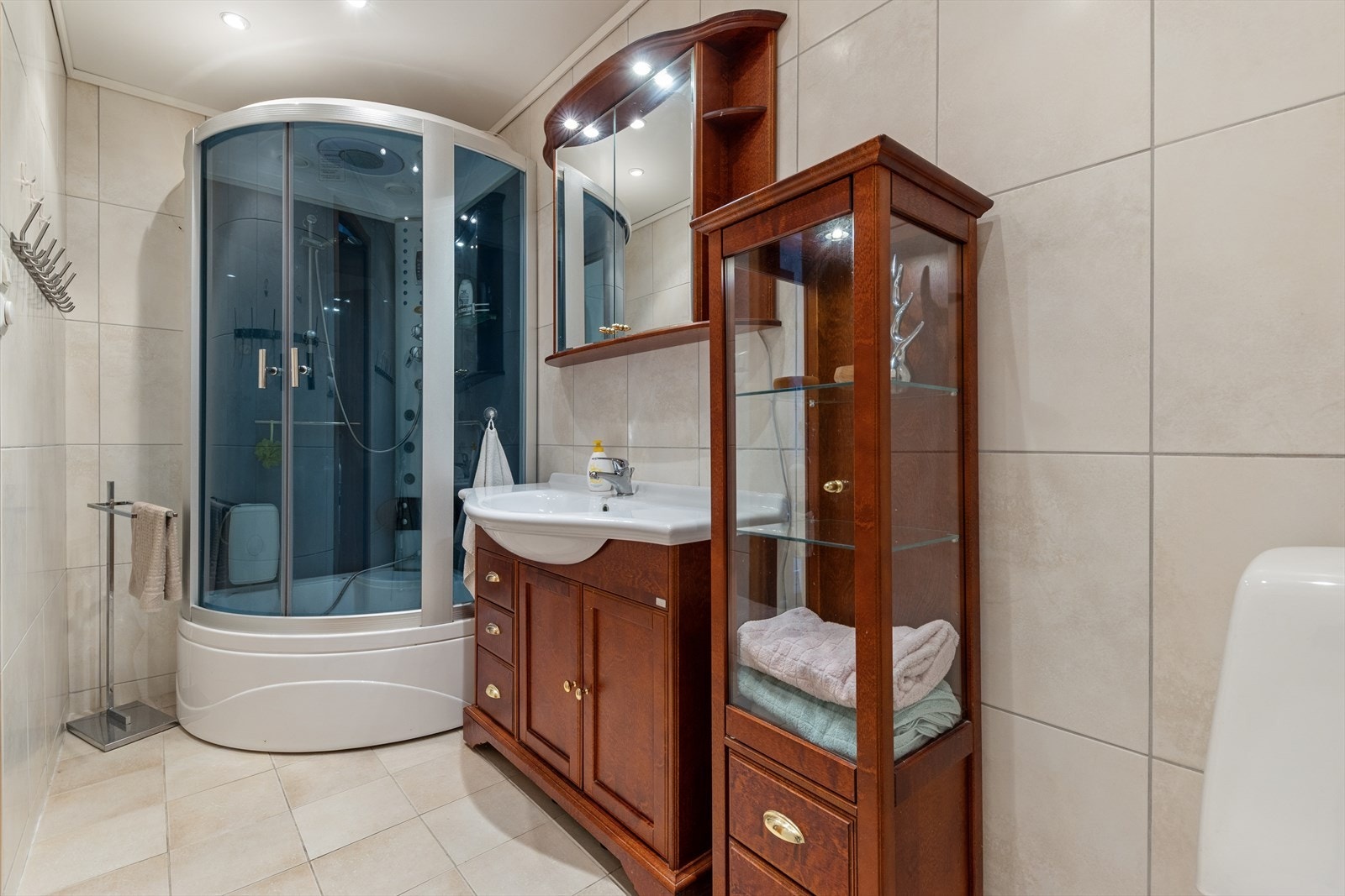 Badet er innredet med en servant nedfelt i baderomsmøbel, et gulvstående toalett og et dusjkabinett. Galleribilde