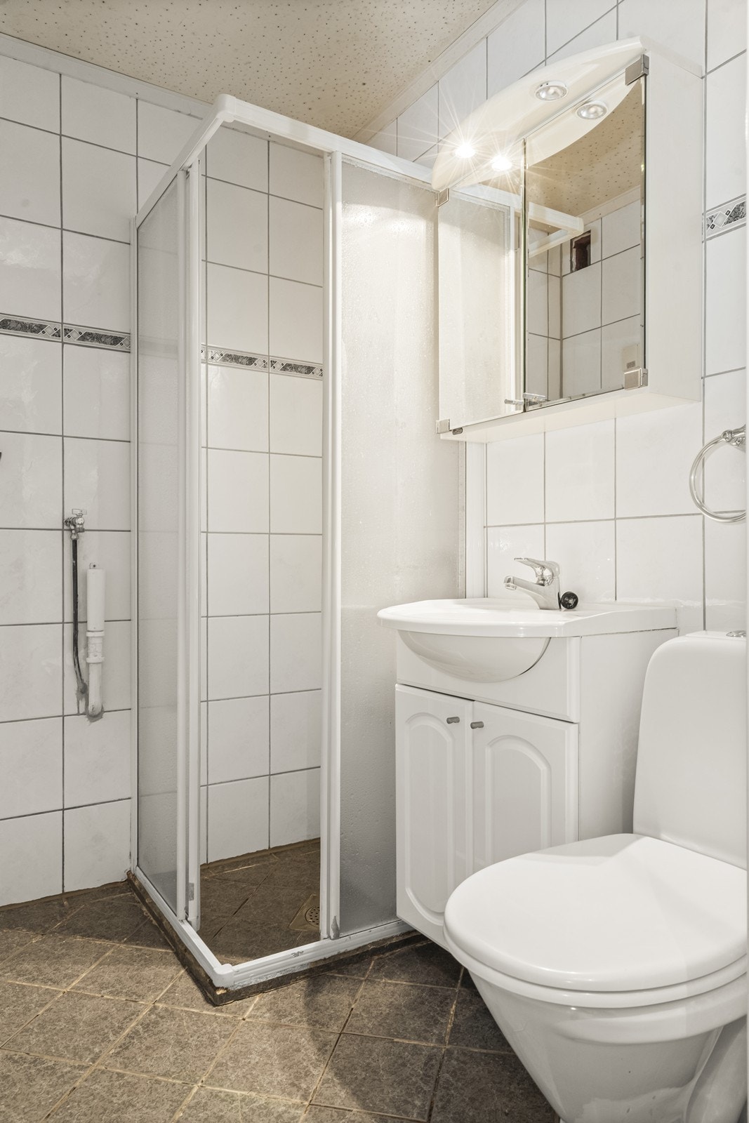 Flislagt bad med dusjkabinett, servant med underskap og toalett. Galleribilde