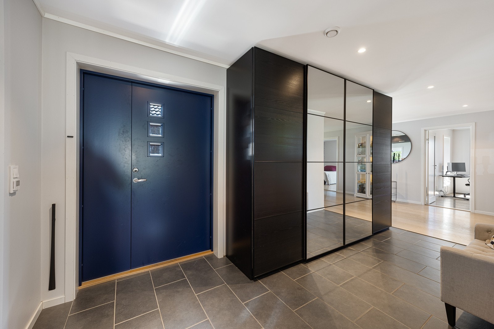 Entreen har lysmalte veggflater, himling med downlights og en stor skyvedørsgarderobe med mørke fronter i trestruktur og speil. Galleribilde
