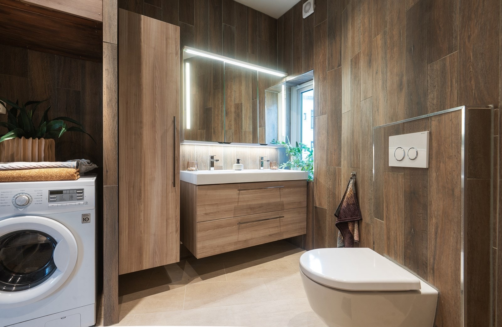 Innredning bestående av glatte fronter som inkluderer benkeskap, veggskap, høyskap med speil og integrert belysning over servant Galleribilde