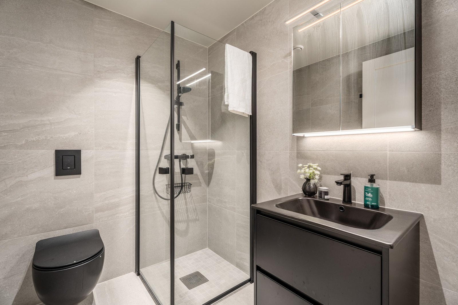 Stilrent helfliset bad (1 av 2) av kvalitet med gulvvarme. Speil med overlys og stikkontakt over servant. Dusjhjørne med dører og vegghengt toalett. Galleribilde