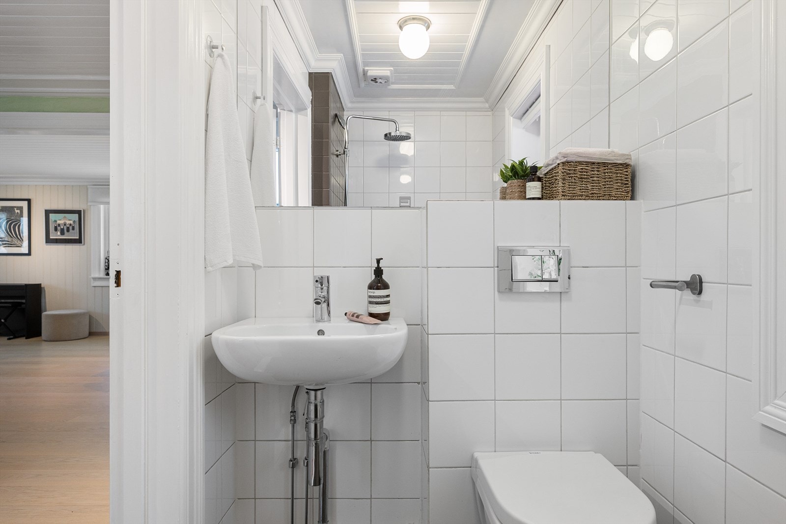 Badet er innredet med veggmontert toalett, dusjhjørne samt servant med tilhørende skap, speil og belysning. Galleribilde