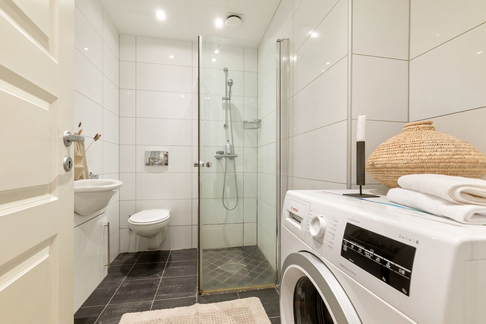 Romslig flislagt bad utstyrt med toalett, dusjhjørne med glassdører og servantskap. Galleribilde