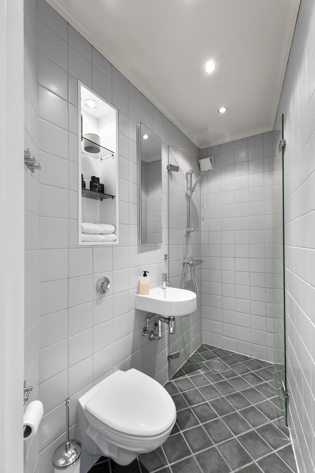 Flislagt bad med dusjsone, varme i gulvet, vegghengt toalett og servant samt nisje i vegg Galleribilde