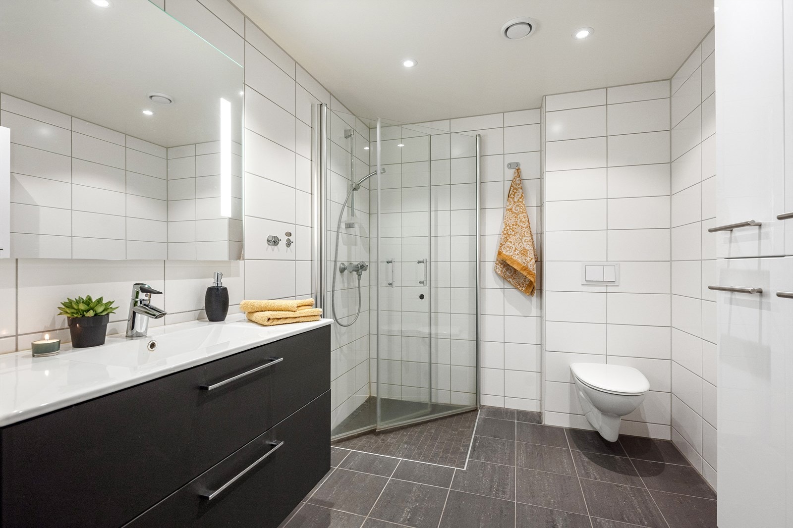 Badet i 1. etasje har et moderne uttrykk med mørke fliser på gulvet og mosaikkfliser i den nedsenkede dusjsonen. Det er varme i gulvet. Galleribilde