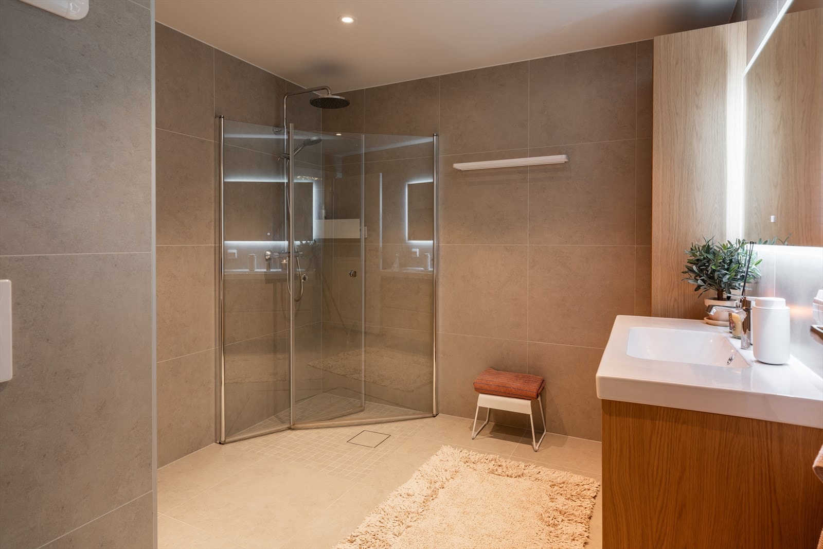 Badet er videre utstyrt med vegghengt klosett med innebygd sisterne og en dusjsone med innfelte dusjdører i herdet glass, som bidrar til et luftig og ryddig preg. Galleribilde