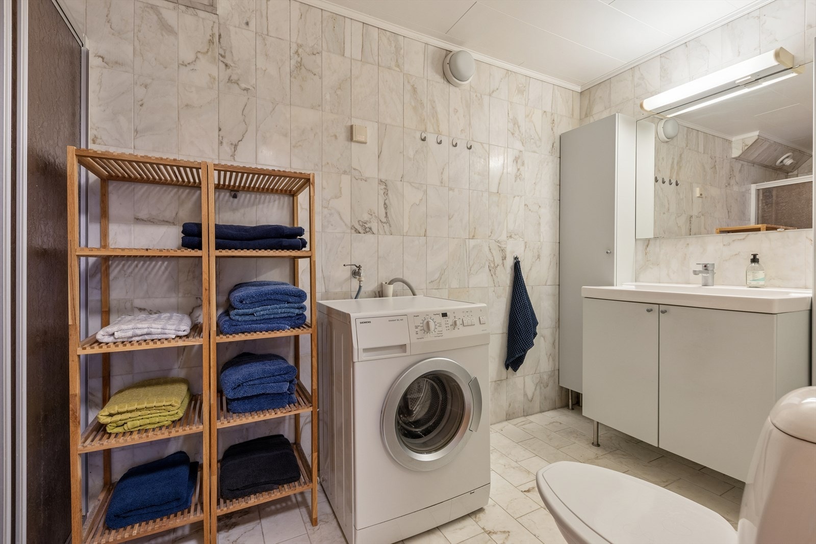 Baderommet i kjelleren er av eldre dato og er innredet med lyse, sjatterte fliser på gulv og vegger. I gulvet har man også varmekabler. Badet er ellers utstyrt med dusjhjørne, toalett, baderomsinnredning med servant og opplegg for vaskemaskin. Galleribilde