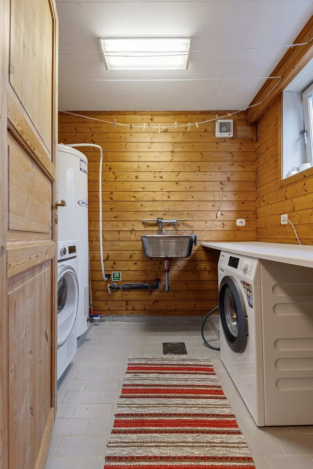 I kjelleren finner man også et vaskerom som er innredet med flislagt gulv og panel på vegg. Rommet er ellers utstyrt med utslagsvask, varmtvannsbereder og opplegg for vaskemaskin. I tillegg har man gode arbeidsflater på benk. Galleribilde