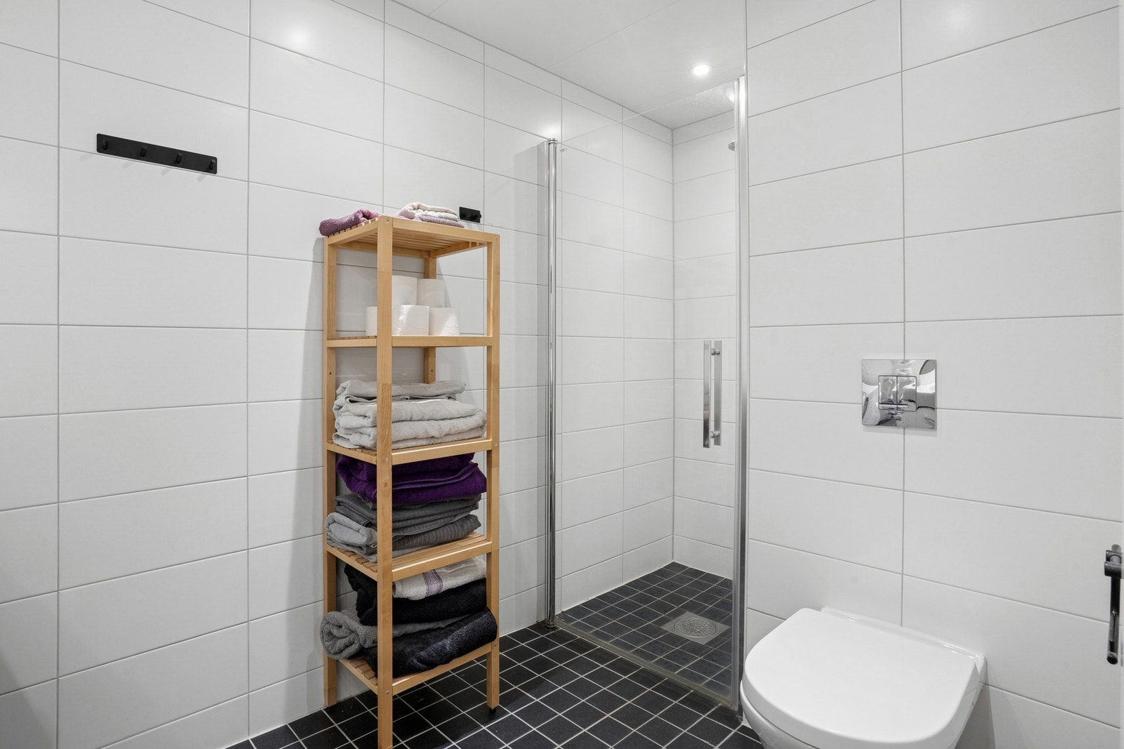 Dusj på gulv med glassdør. Dusjarmatur tilkoblet veggmontert hånddusj. Vegghengt toalett med innebygget sisterne. Galleribilde