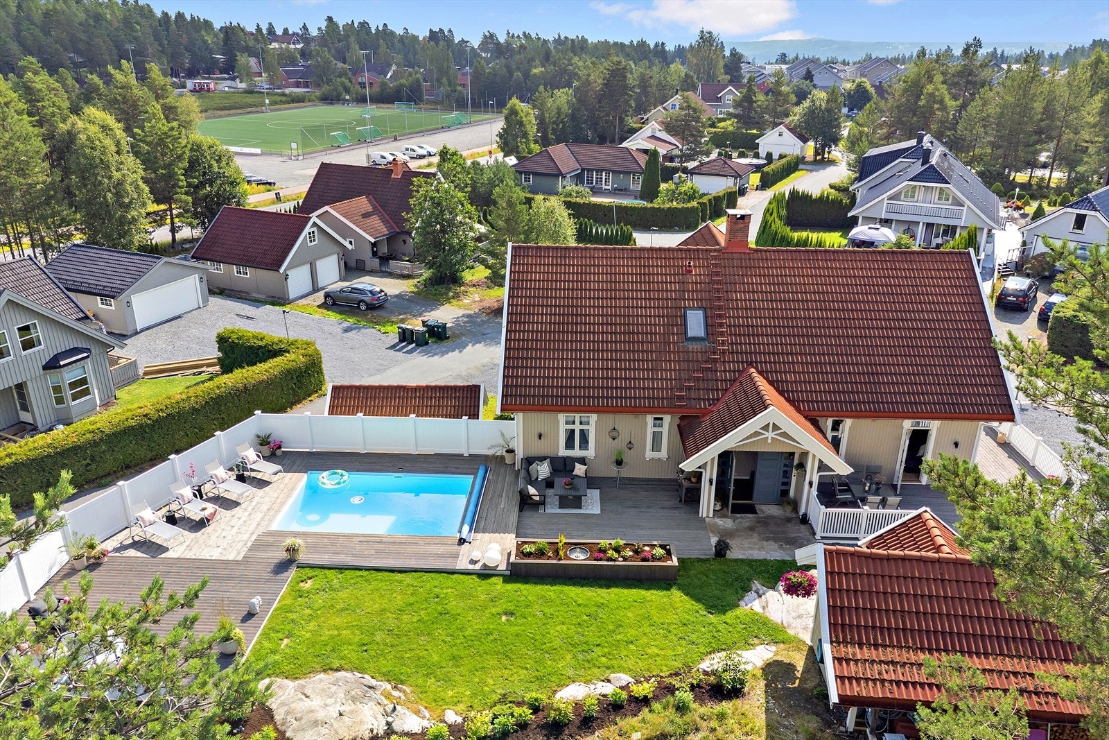 Stor tomt som er opparbeidet med gruset gårdsplass og hage. Grenser mot skog. Opparbeidet terrasseanlegg med nedsenket basseng. Galleribilde