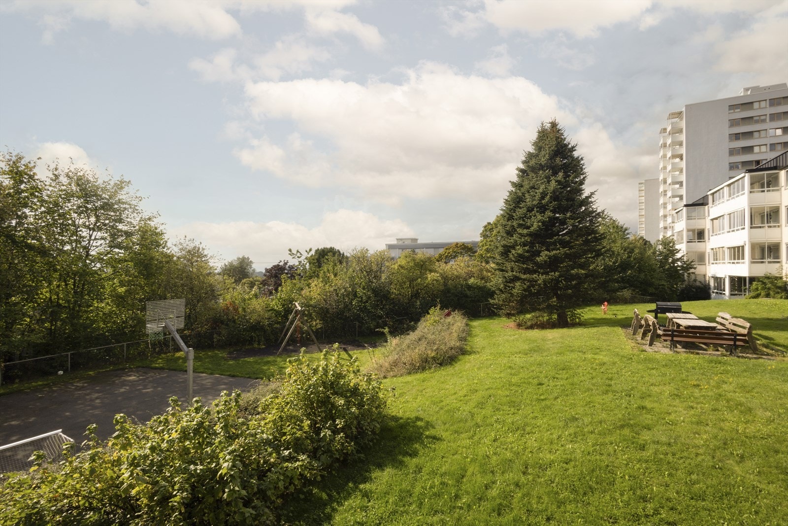 Utsikt fra balkongen mot basketballbane, lekeplass, grøntareal og sittegrupper. Galleribilde