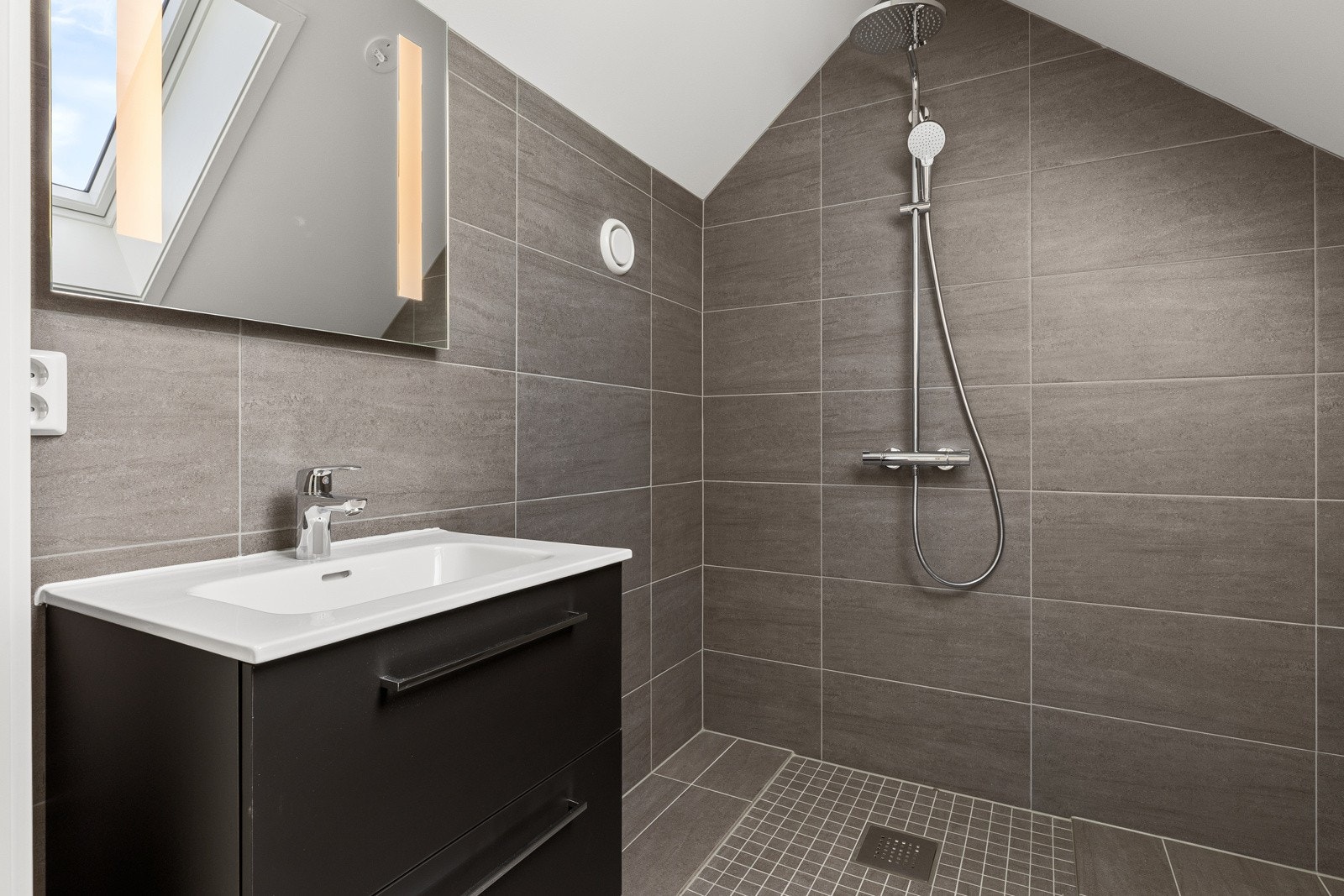 Badet på loftet er delikat med store mørke fliser og gulvvarme Galleribilde