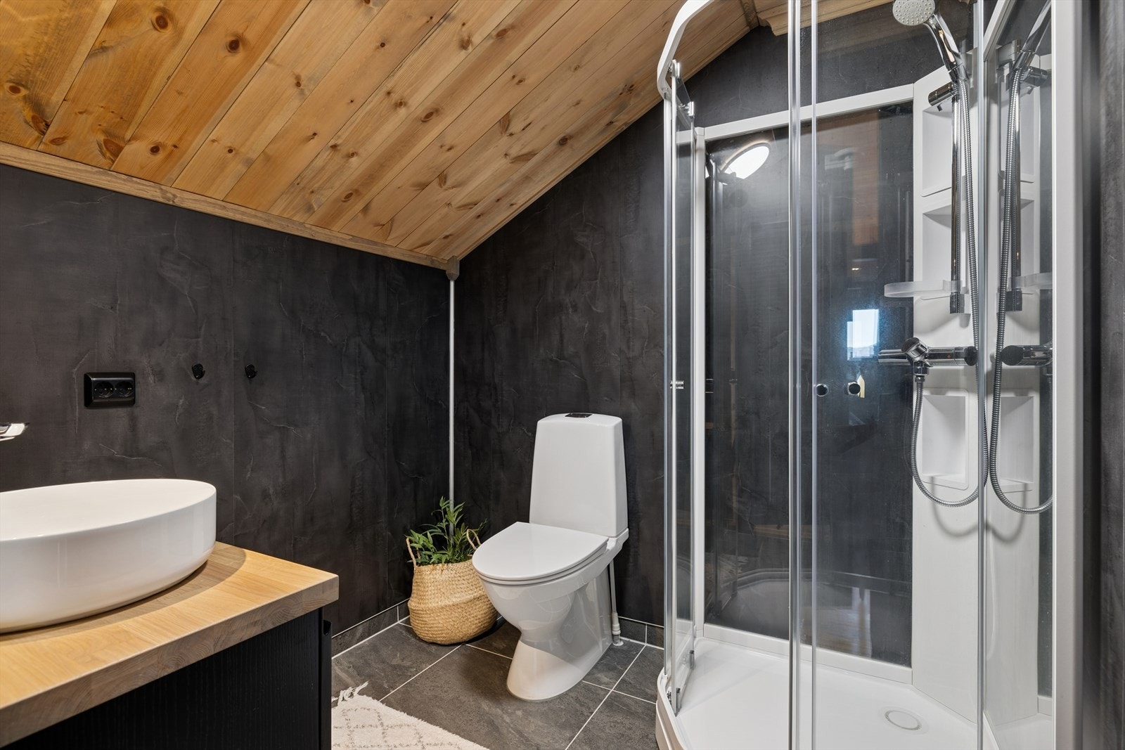 Bad i 2.etg som fremstår som praktisk og gjennomført, med materialvalg som gir både komfort og et helhetlig inntrykk. Her finner du et gulvstående toalett, dusjkabinett og et servant skap med vask i en stil som harmonerer med resten av hytta. Galleribilde