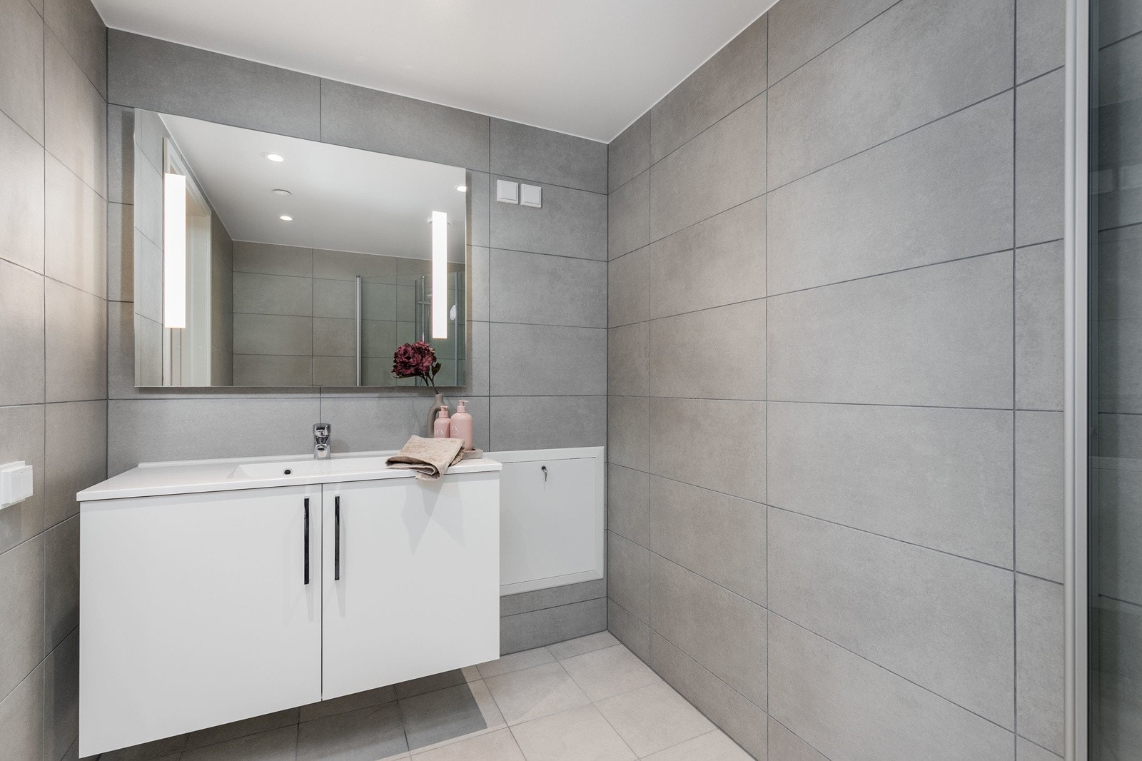 Delikat flislagt bad med vegghengt toalett, dusjsone med innfellbare dører samt servant med skapinnredning. Bilde fra L707 Galleribilde