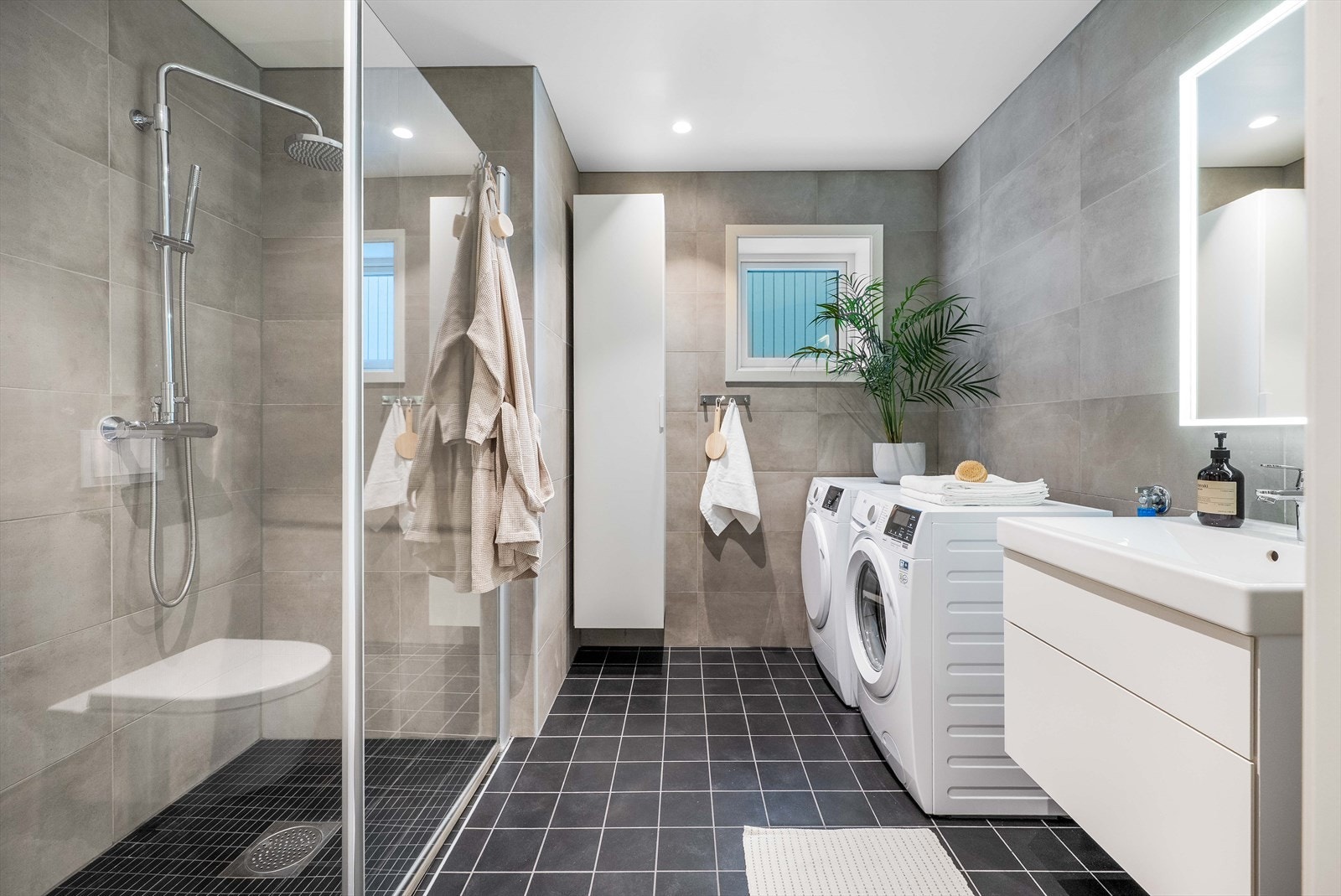 Det andre badet i 2. etasje er stort og praktisk innredet med mørke fliser på gulv med underliggende varme og grå fliser på vegger. Badet er videre innredet med regnfallsdusj, heldekkende servant og speil med belysning Galleribilde