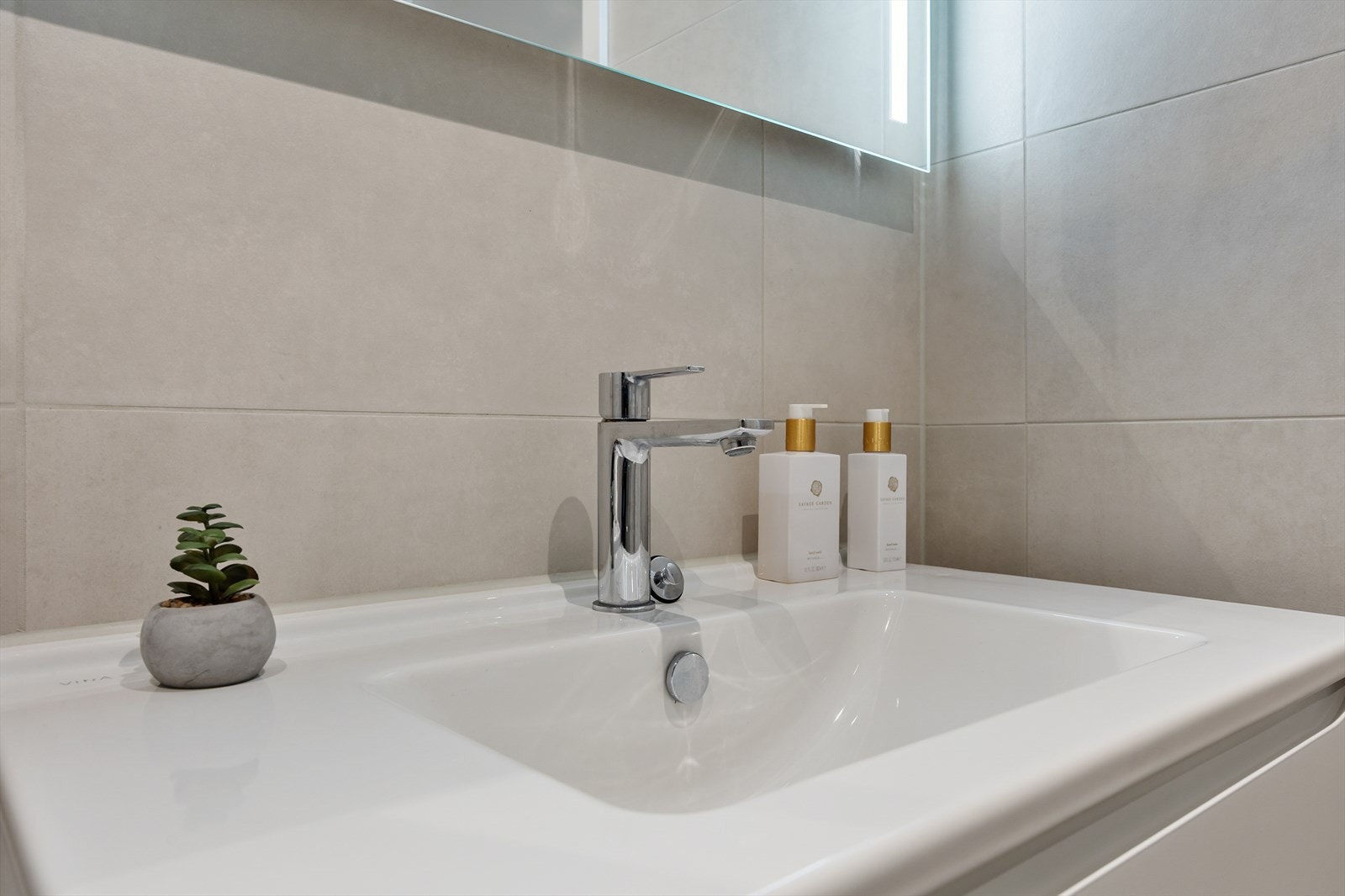 Badet er innredet med servant i innredning med skuffer, vegghengt toalett, dusjhjørne og opplegg for vaskemaskin Galleribilde